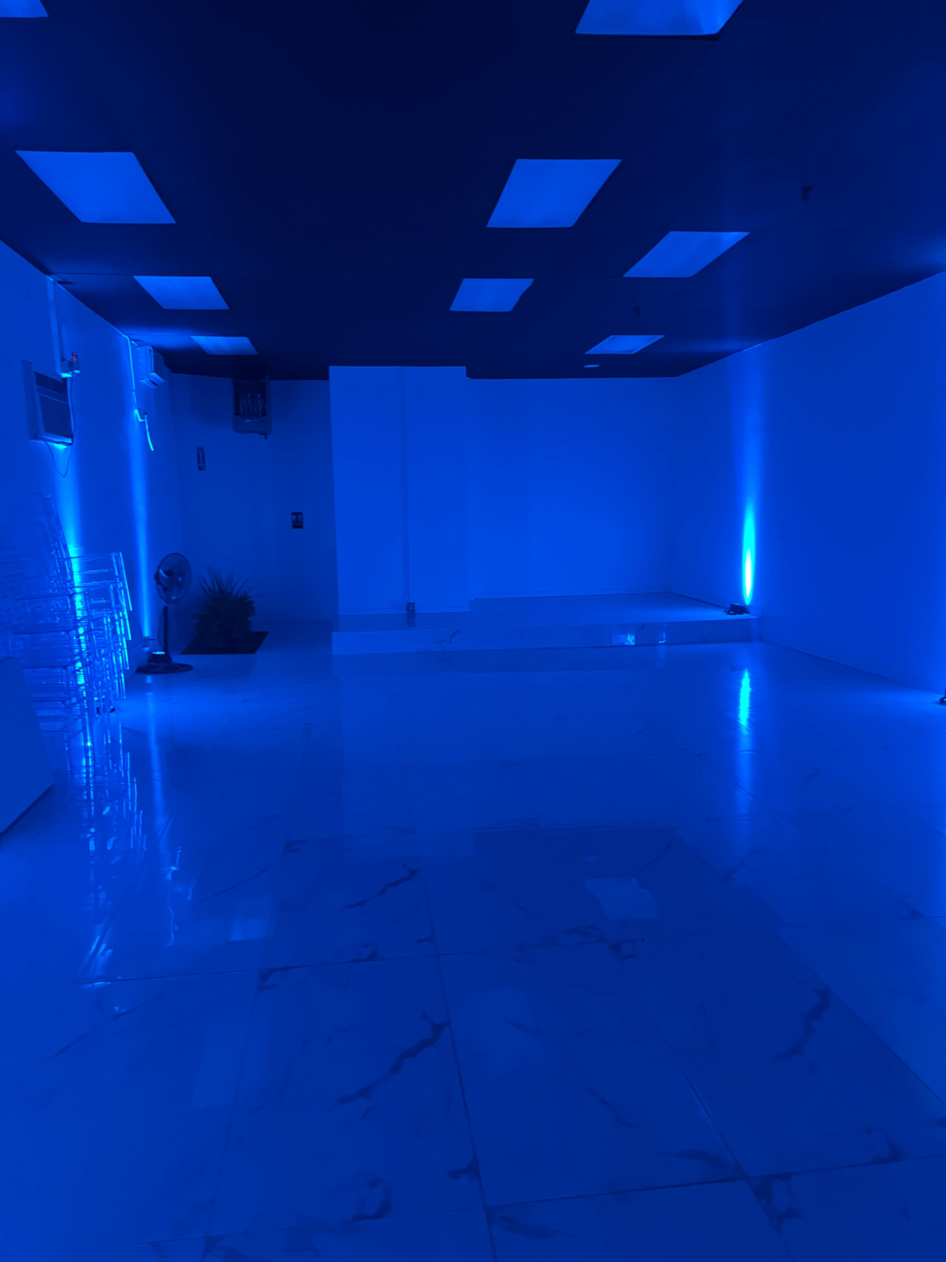 A dimly lit room with blue walls and lighting, featuring a shiny marble floor and minimal furnishings.