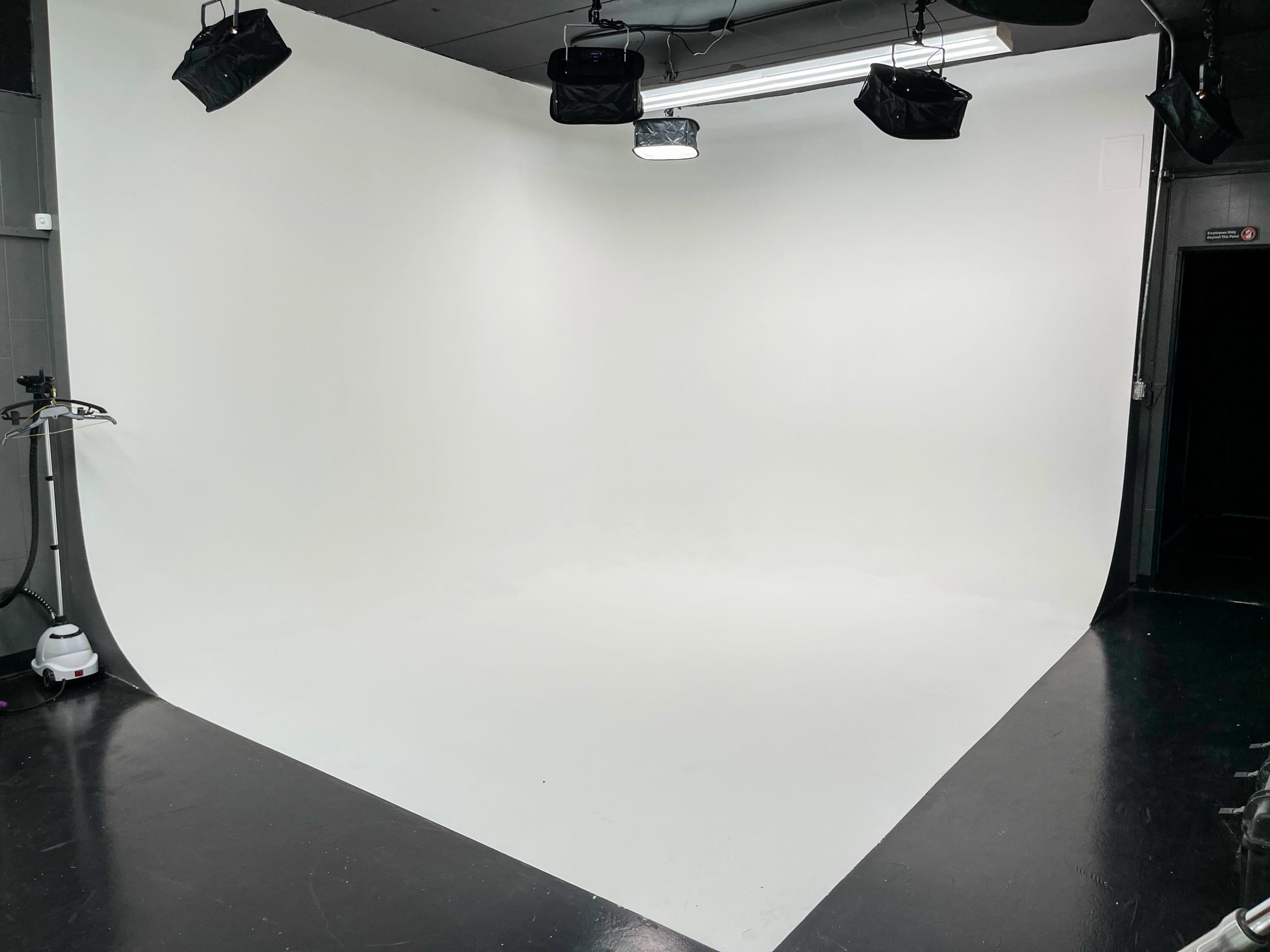 The image shows a photography studio with a seamless white backdrop and overhead lighting.
