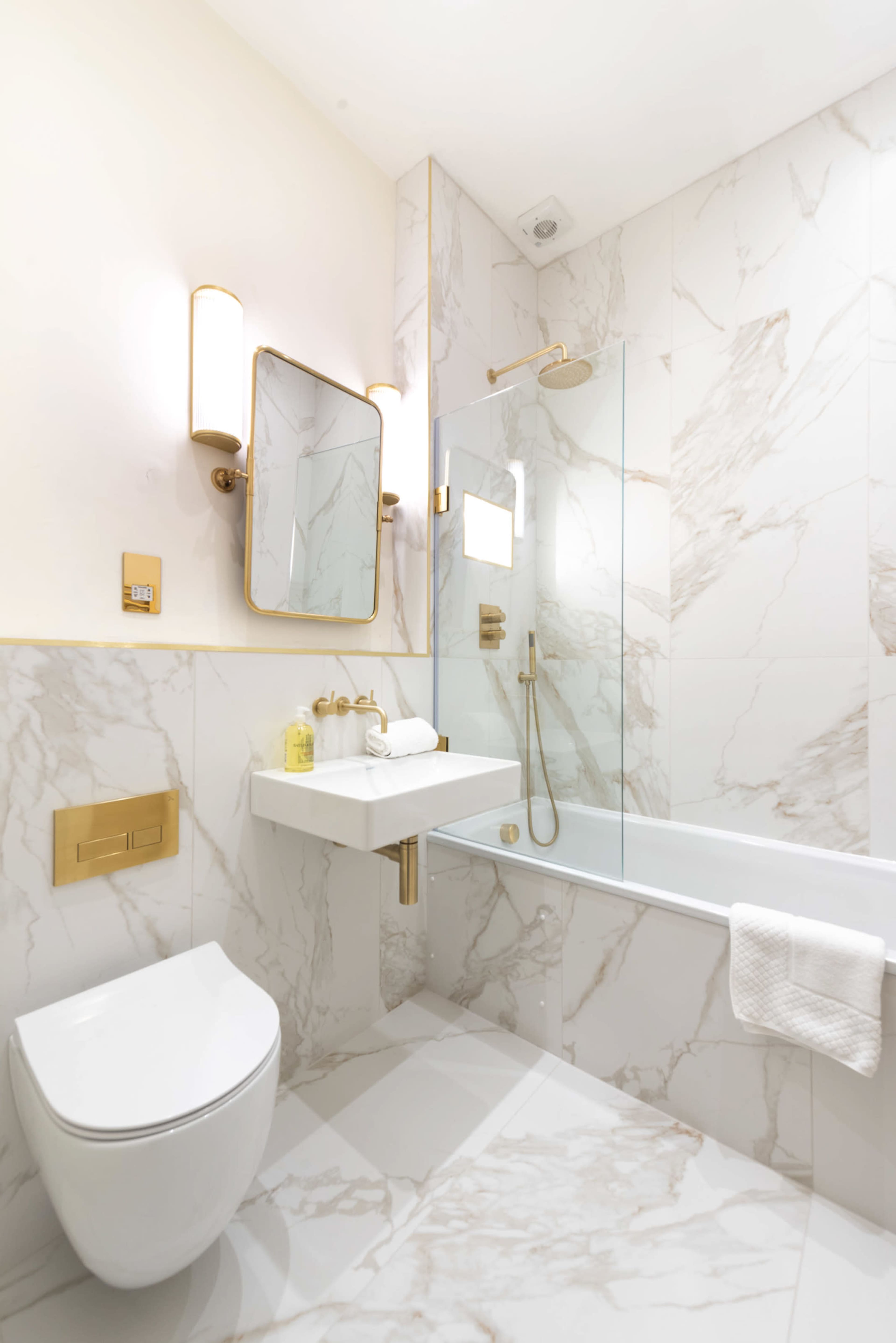 The bathroom features marble walls, a glass shower enclosure, a modern toilet, and a wall-mounted sink with gold accents.