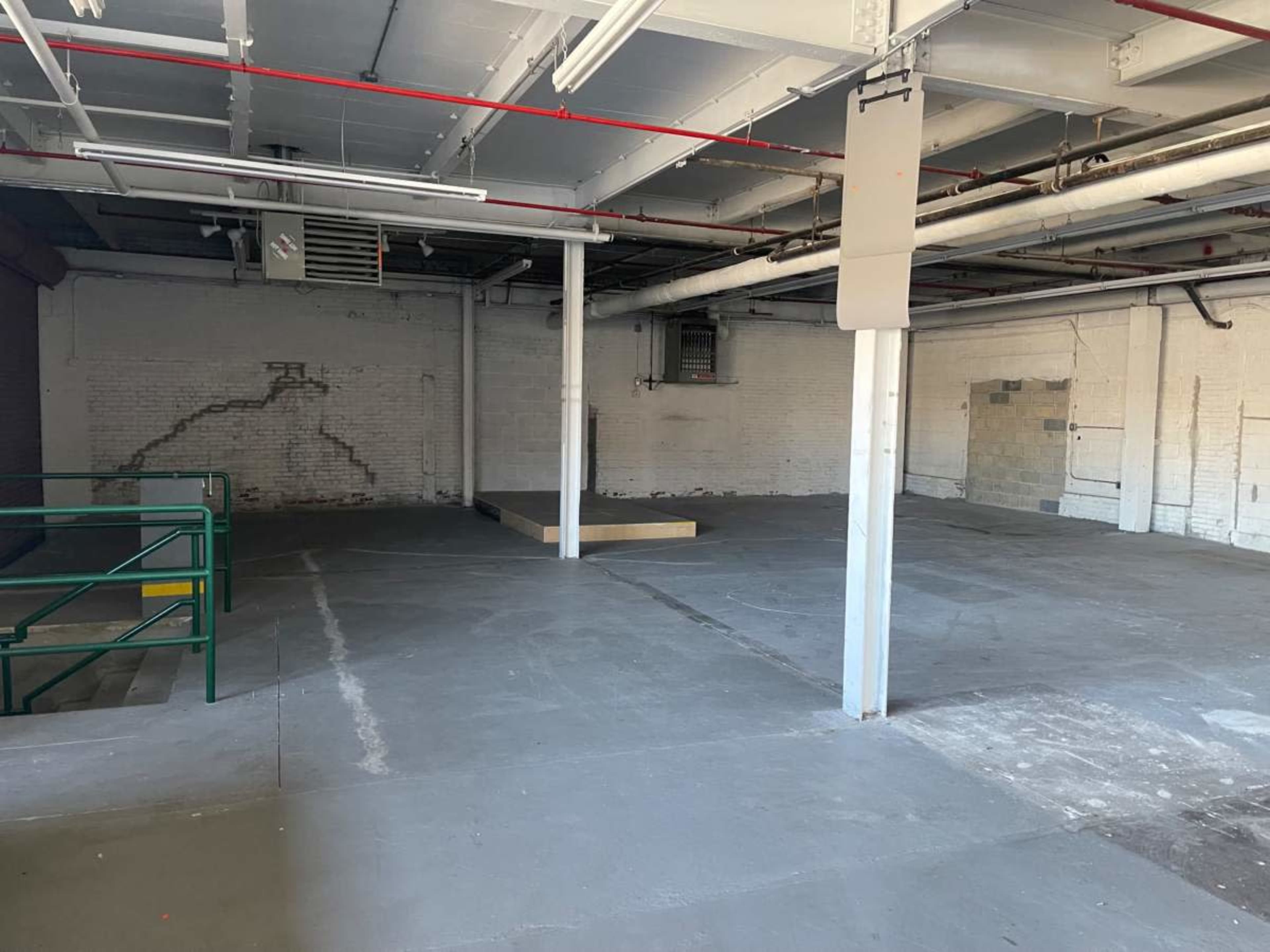 The image shows an empty industrial space with bare concrete floors, exposed pipes, and minimal lighting.
