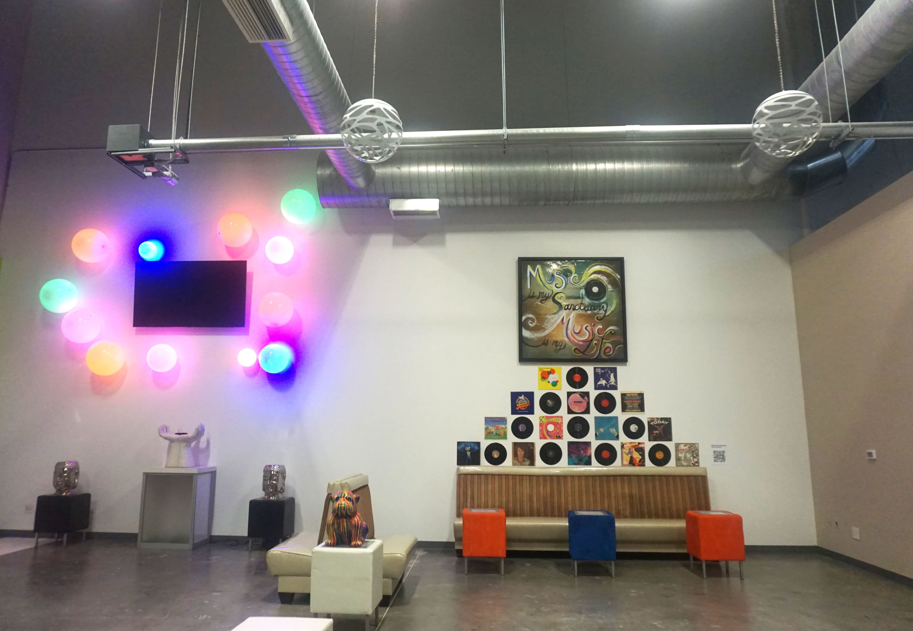 A modern lounge with colorful decorative spheres on one wall, a TV mounted above, an artistic vinyl display on another wall, and contemporary seating arrangements.