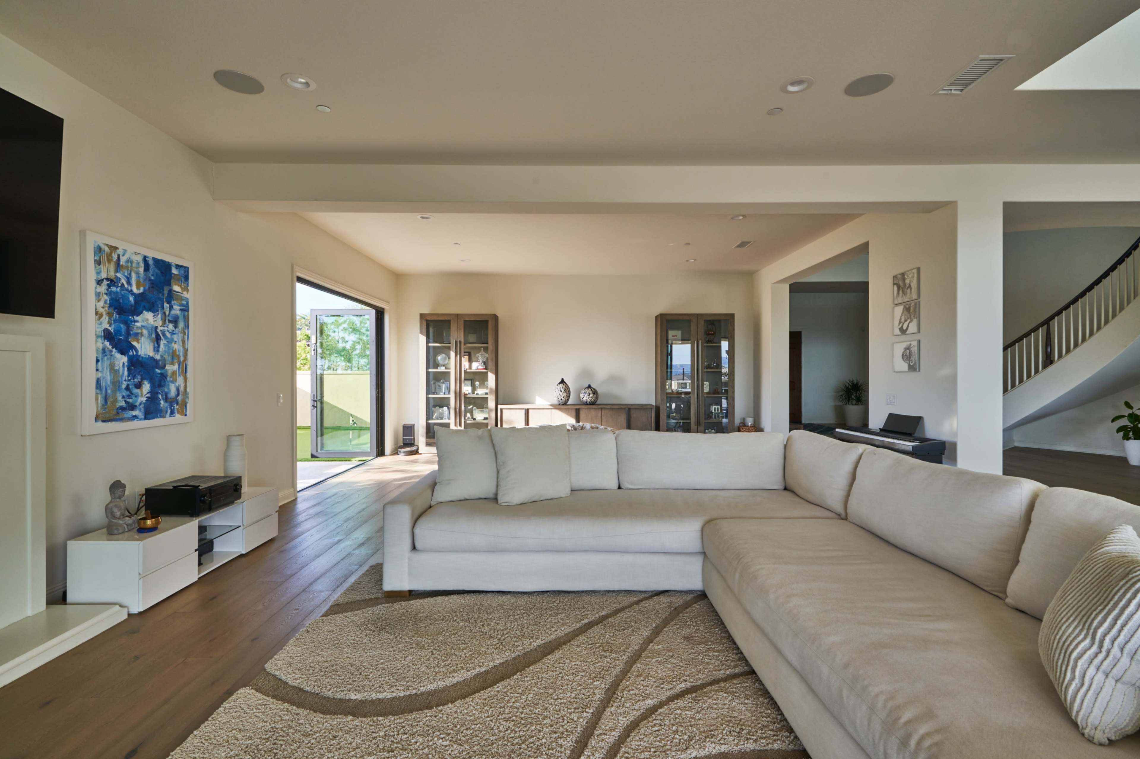 A light-filled, modern living room features a large sectional sofa and an open view to a patio through sliding glass doors.