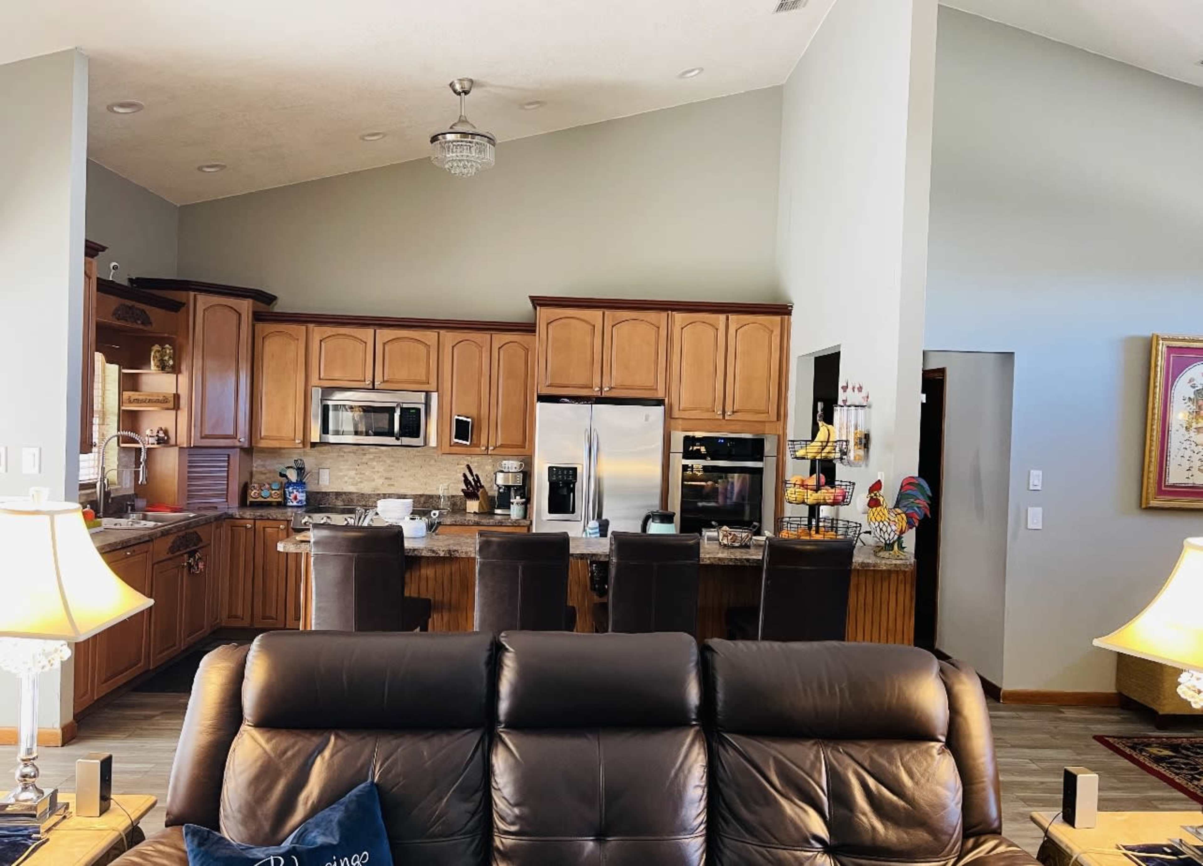 A living room with a leather sofa facing an open kitchen featuring wooden cabinets and modern appliances.