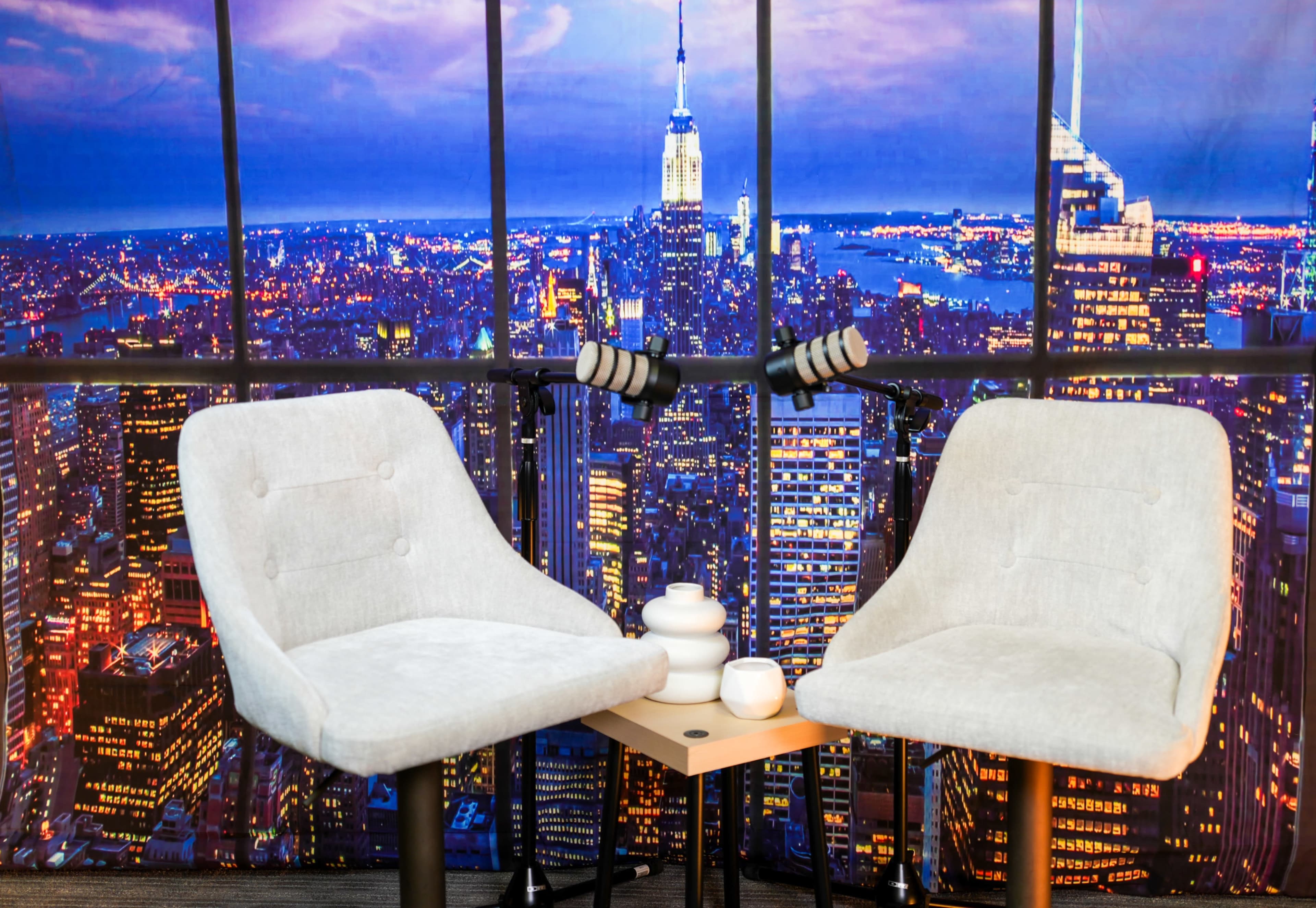 The image shows two gray chairs next to a small table in front of a backdrop featuring a city skyline at night, with the Empire State Building visible.