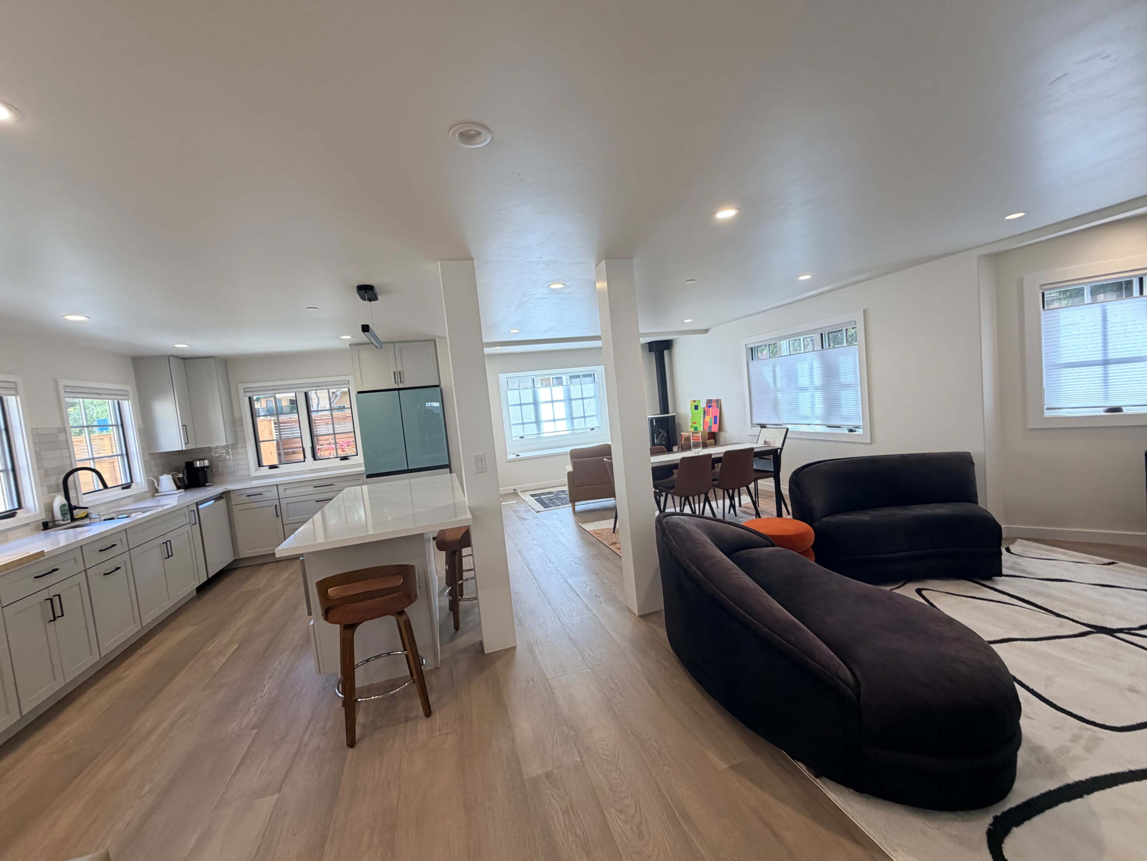 The image shows a modern, open-concept living space featuring a kitchen area with a large island, and a combined dining and living area with a sectional sofa and a dining table.
