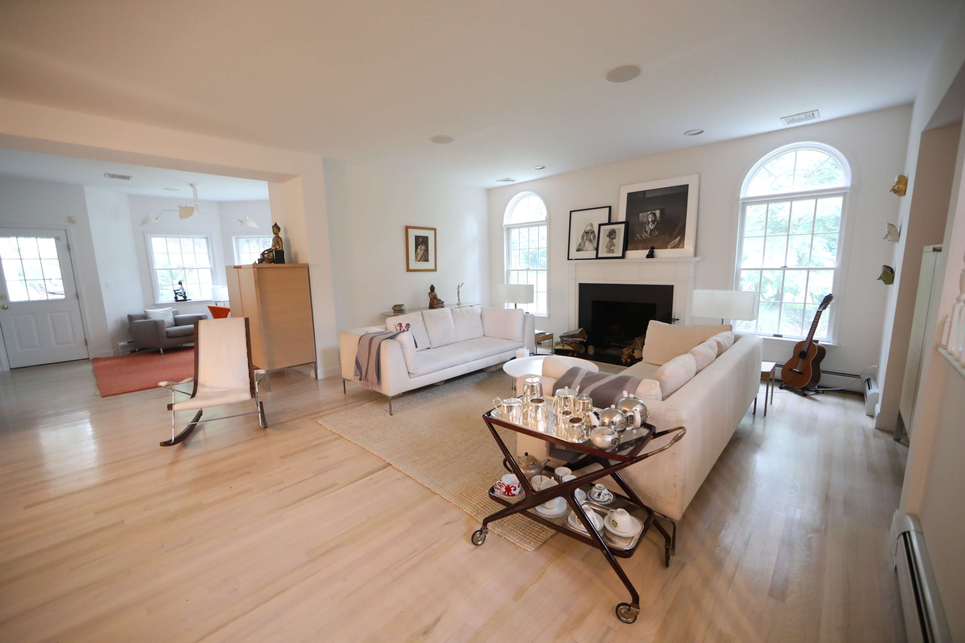 The image shows a spacious living room with a light-colored sofa, a coffee table on a rug, and large windows letting in natural light.