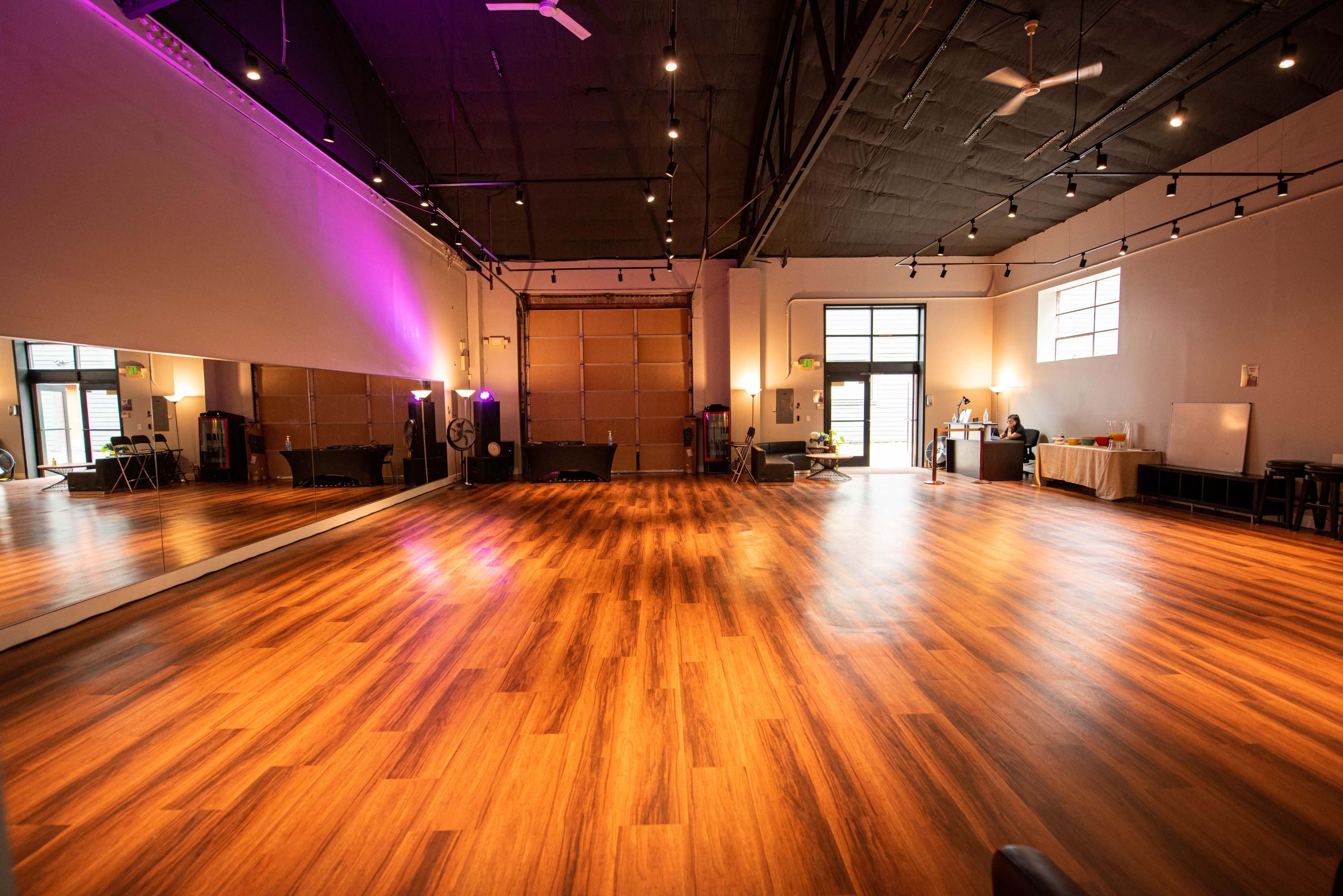 A spacious dance studio with polished wooden floors, large mirrors on one wall, and ample natural light from large windows.