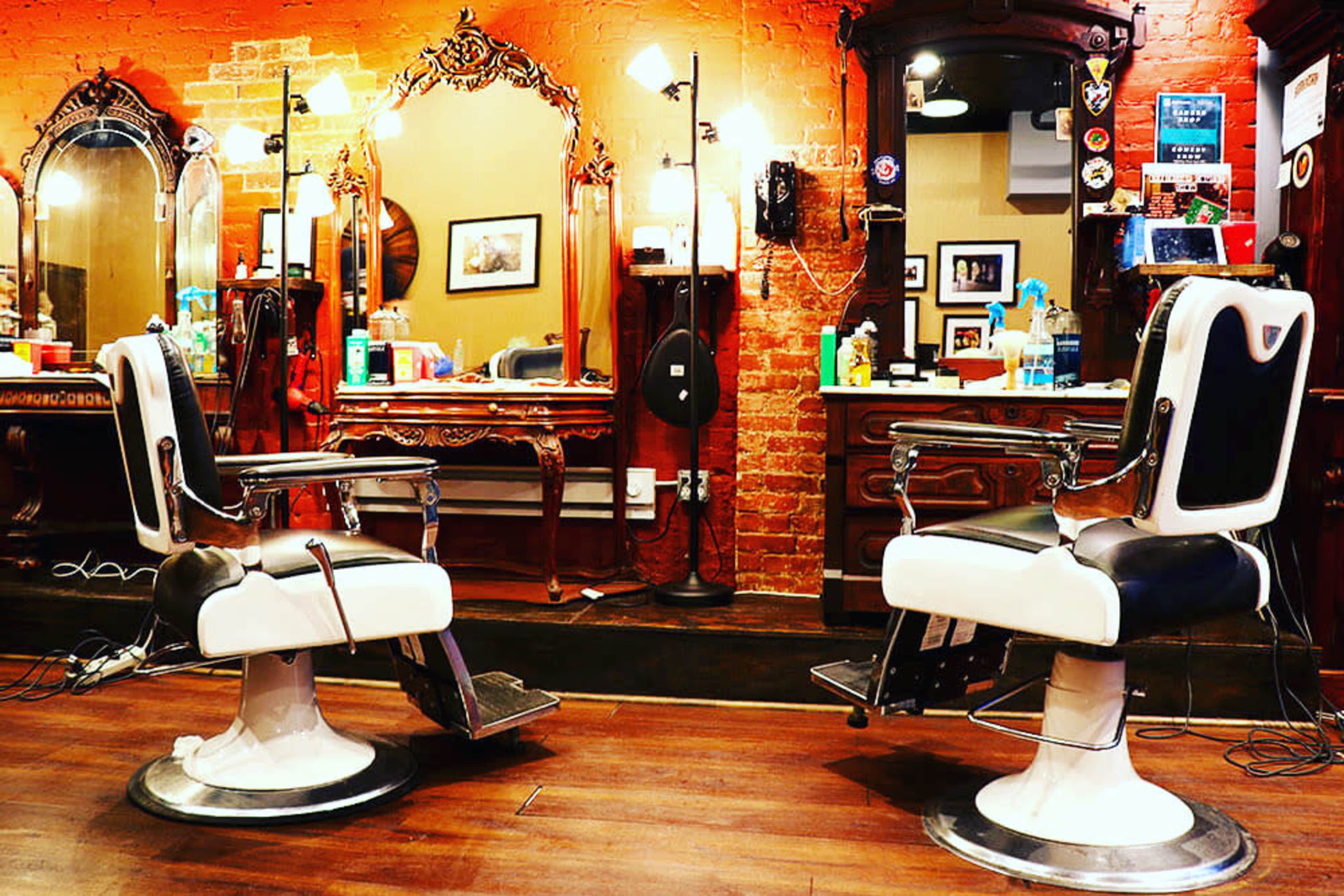 A vintage barber shop interior featuring two black and white barber chairs, ornate mirrors, and brick walls.