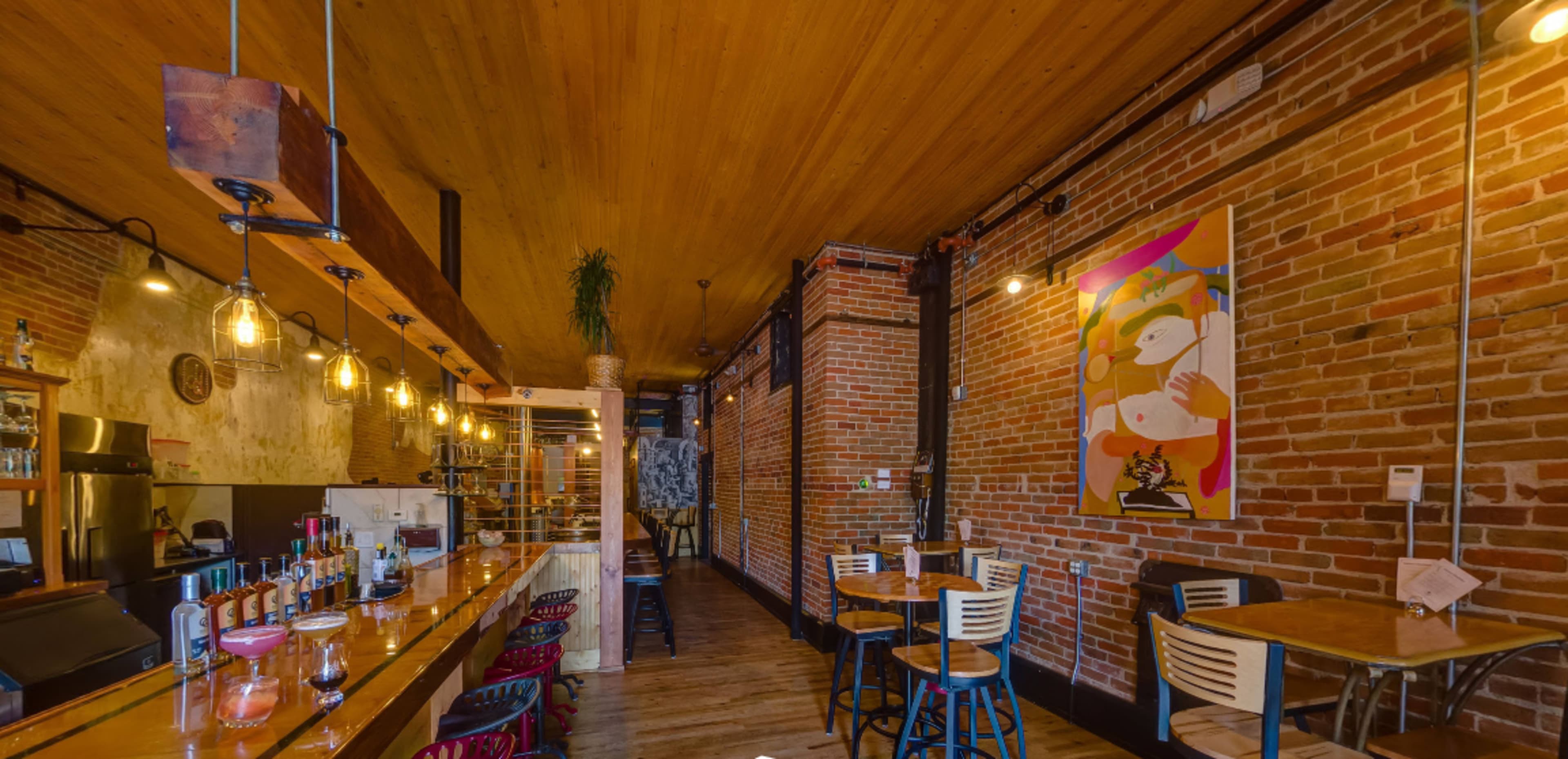 A rustic restaurant interior featuring exposed brick walls, wooden beams, and a long bar with a variety of bottles displayed.