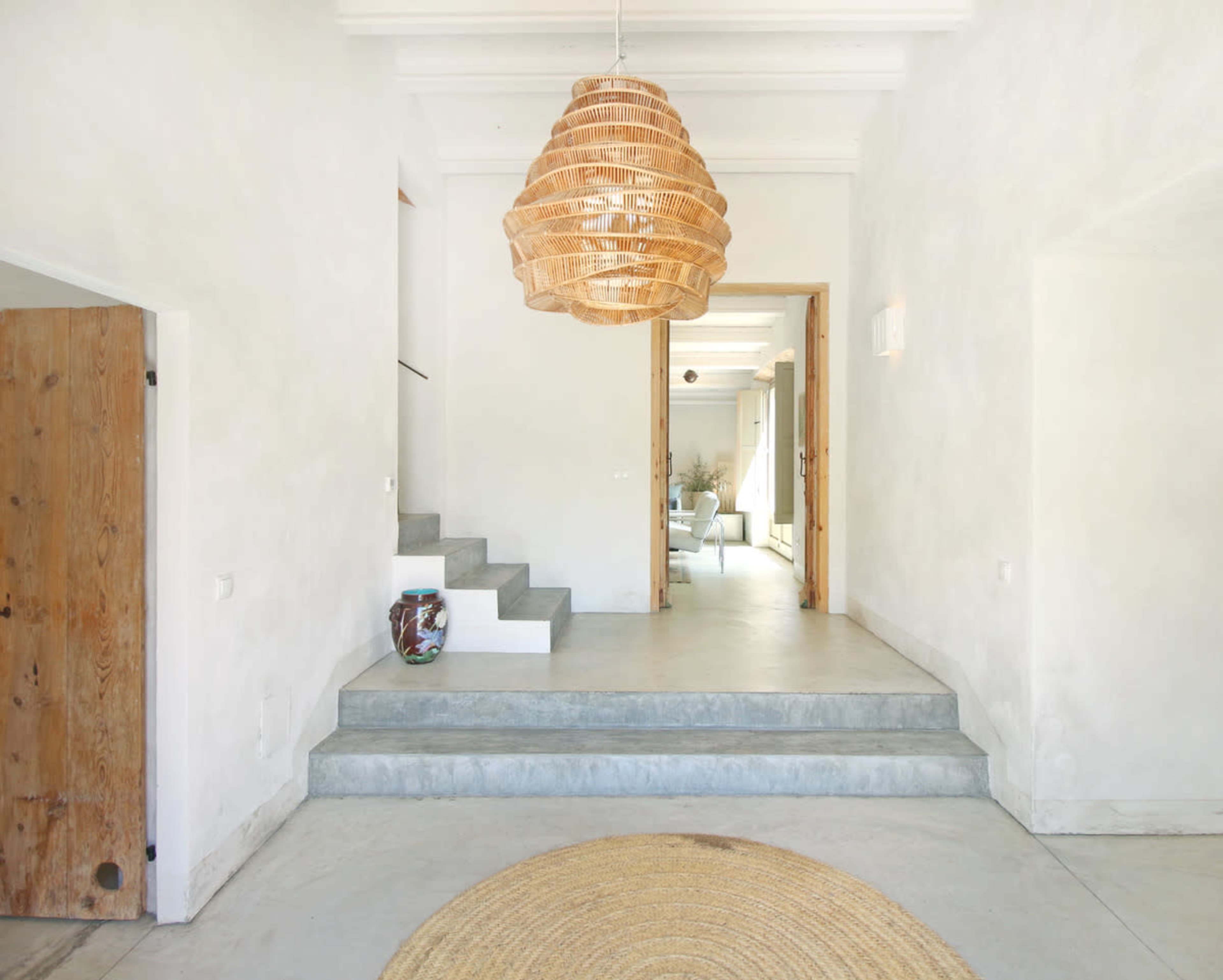 A spacious entrance hall features a woven pendant light, concrete steps, and a circular rug on the floor.