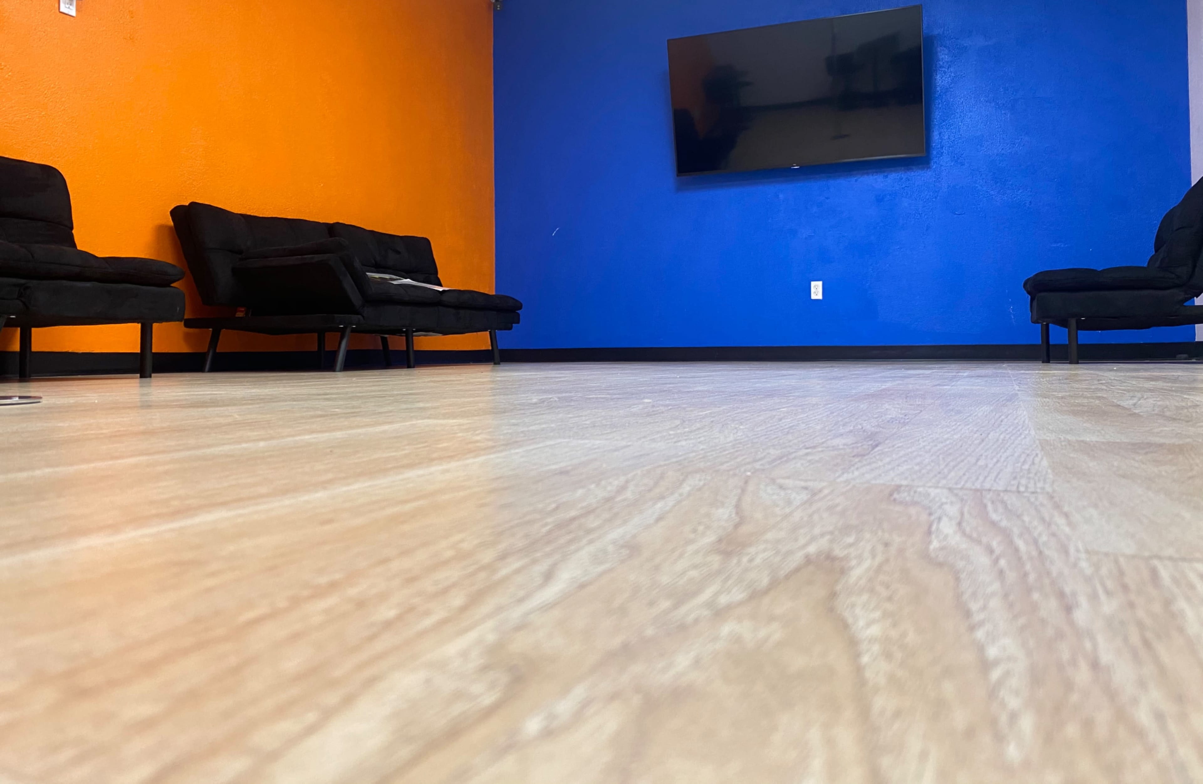 A room with an orange and blue wall, two black couches, and a wall-mounted television.
