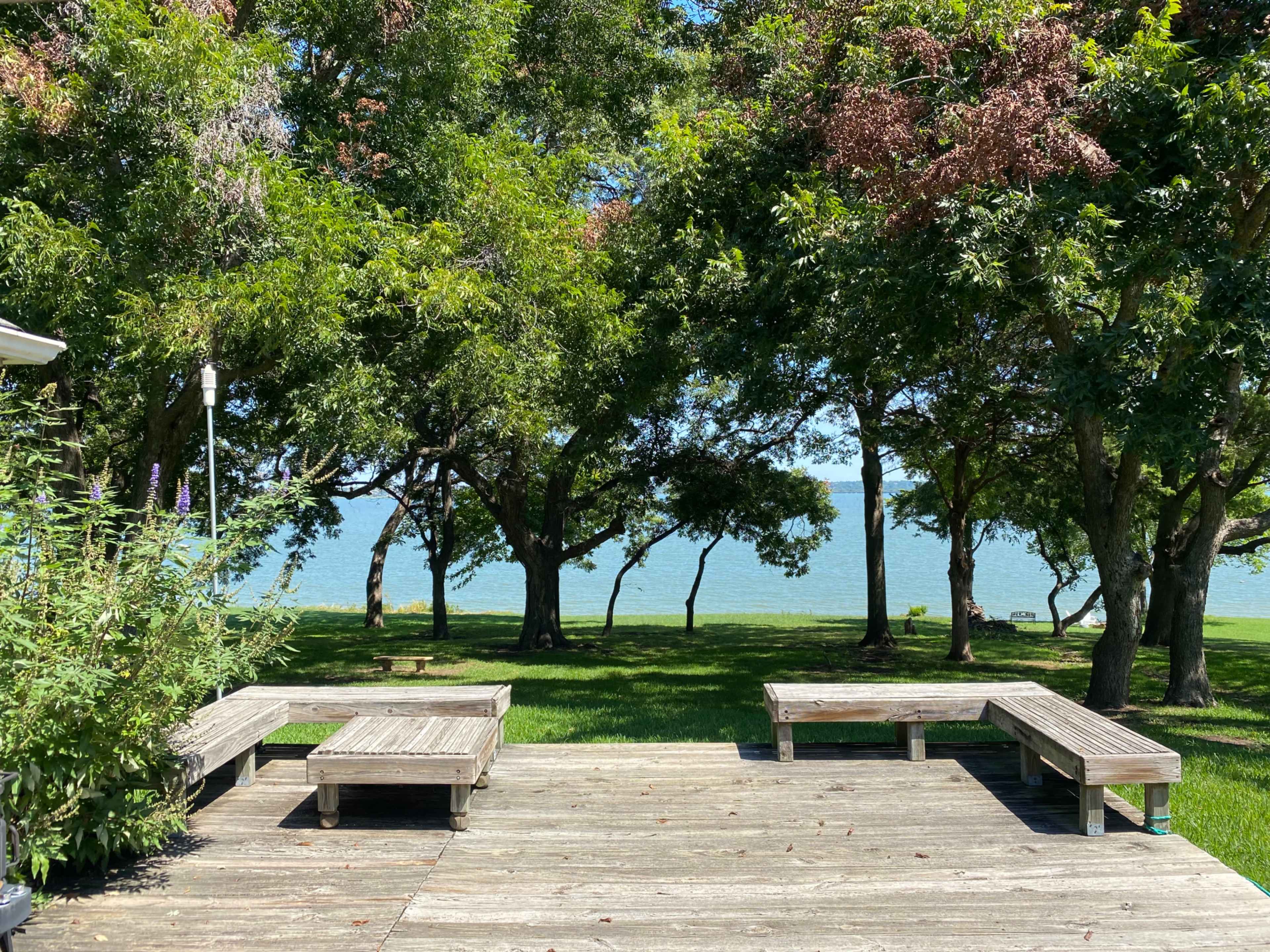 A wooden deck overlooking a grassy area and a body of water, framed by trees.