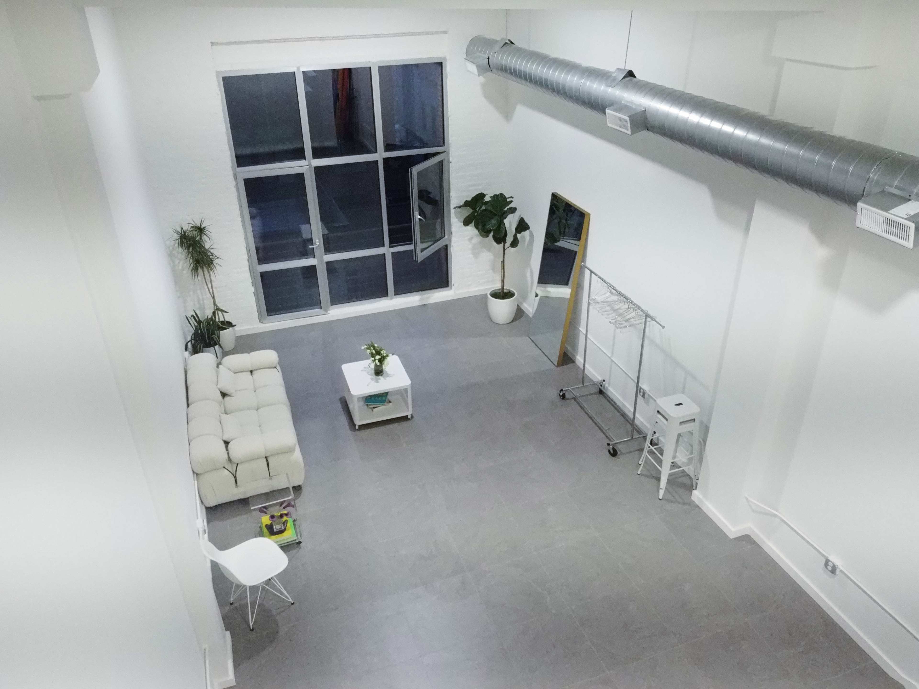 A spacious, minimalist interior with a white sofa, a coffee table, a plant, and large windows allowing natural light.