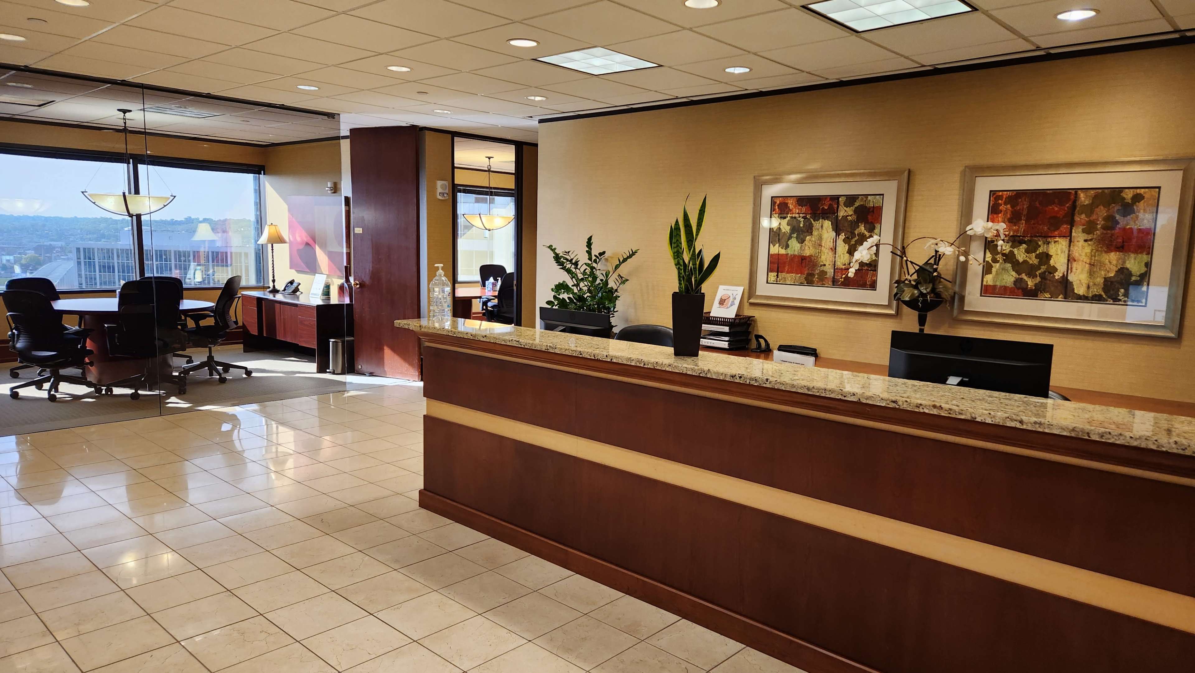 A modern office reception area with a wooden front desk, art on the walls, and seating areas visible through large windows.