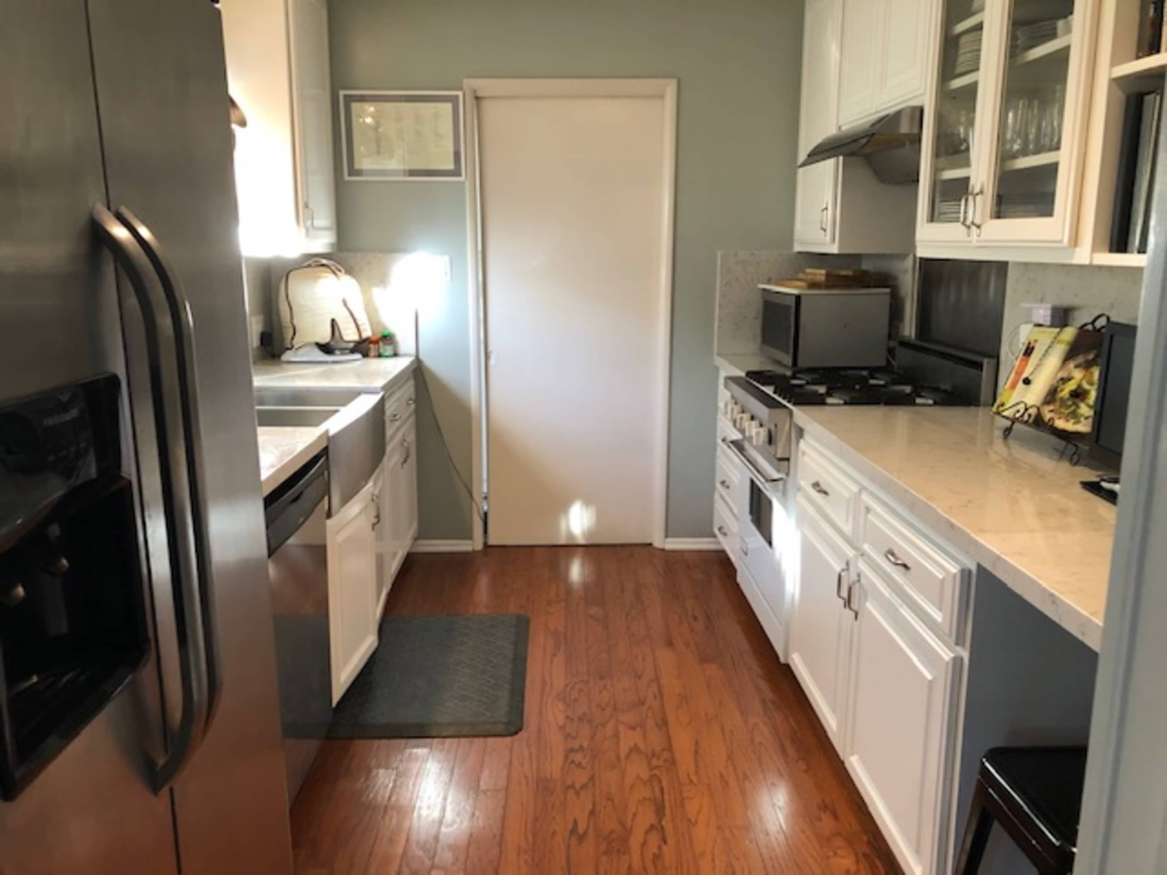 A narrow kitchen with white cabinetry, stainless steel appliances, and a door at the far end leading outside.