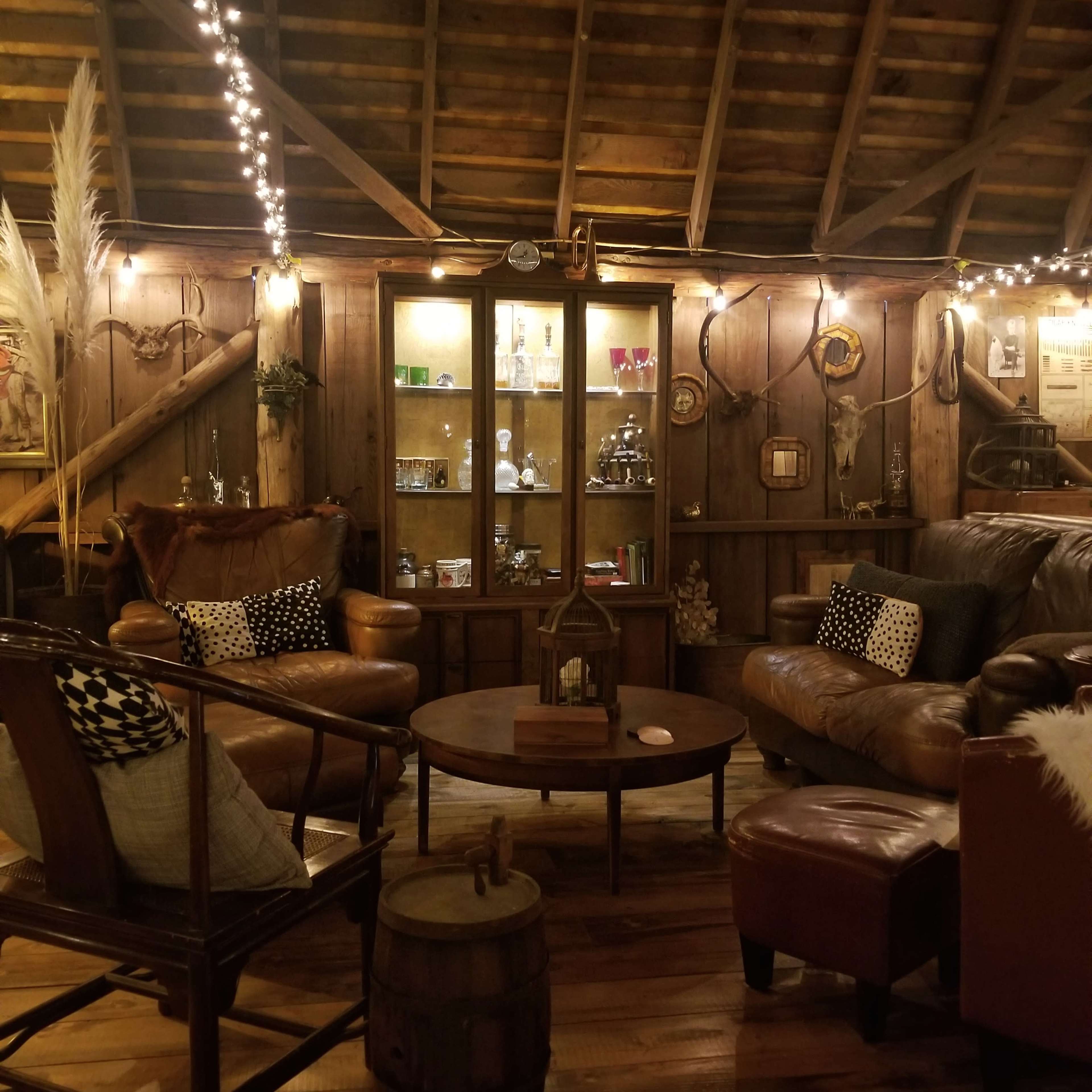 A cozy, rustic living room with wooden walls, soft lighting, and a collection of vintage decor displayed in a glass cabinet.