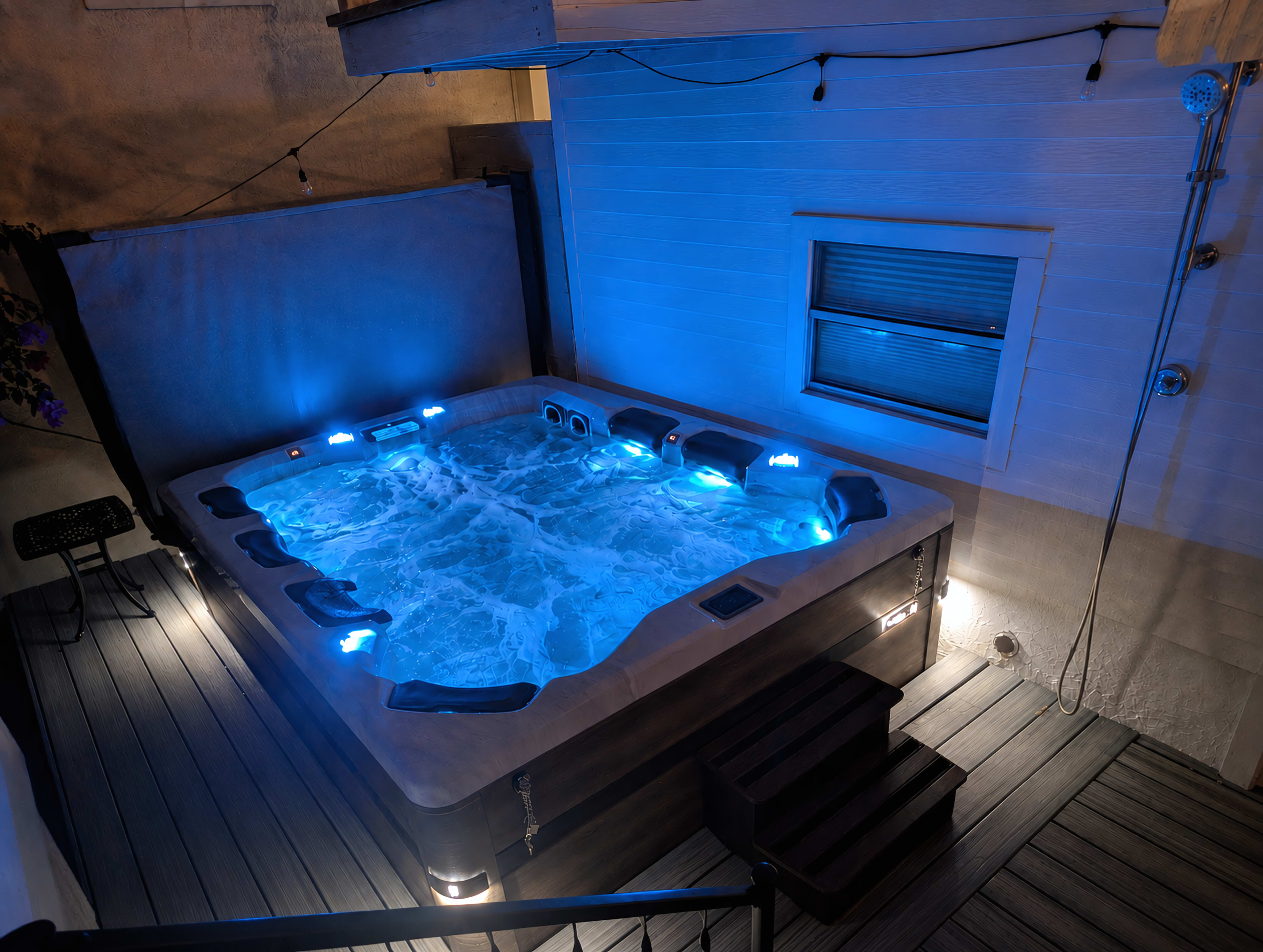 The image shows a hot tub with blue lights, surrounded by wooden decking and a gray wall.