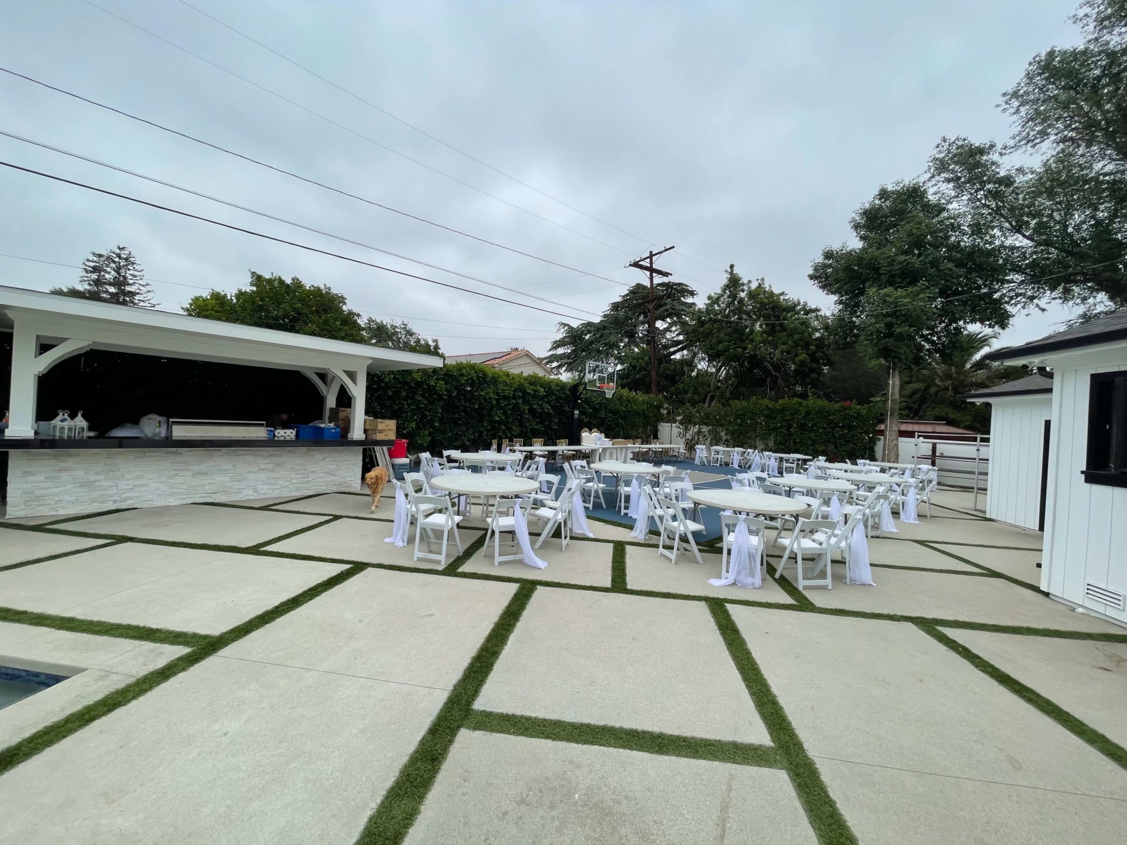 The scene shows a poolside area set up for an event, featuring several tables with white tablecloths and chairs arranged on a concrete surface.