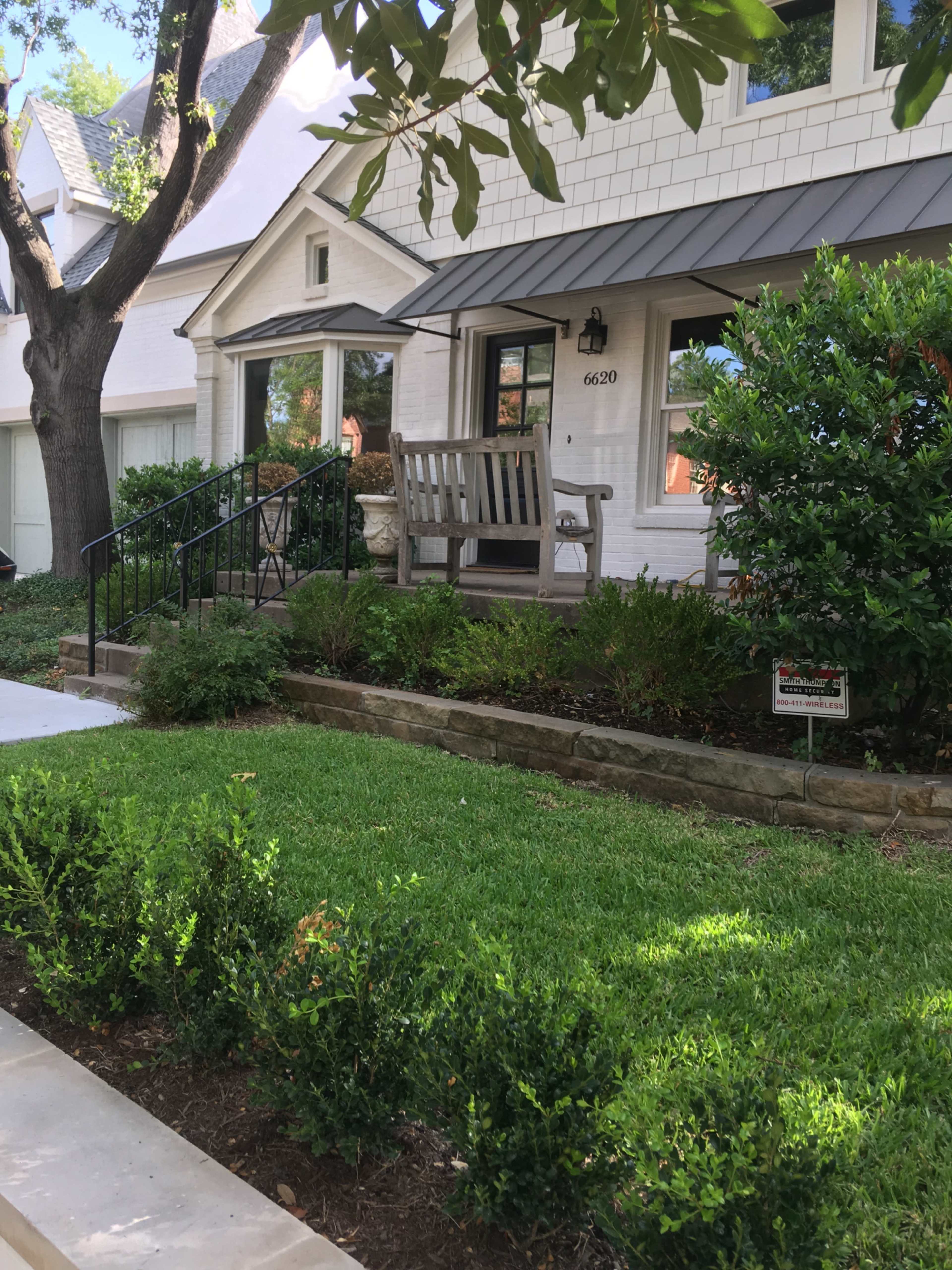 The image shows a front yard of a house featuring a bench, manicured grass, and a pathway leading to the entrance.