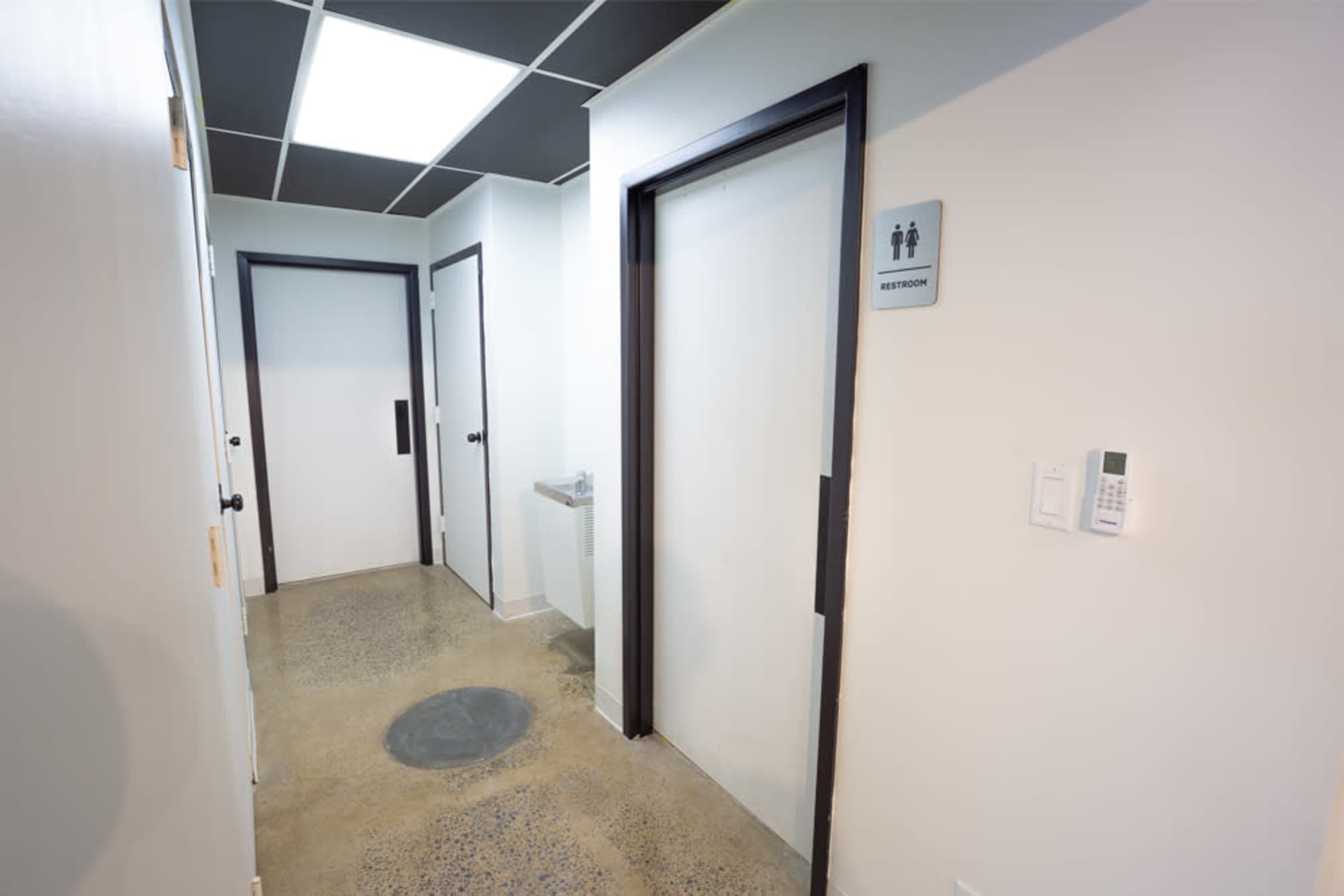 A hallway features two closed doors labeled "Restroom" and a water fountain on the side wall.