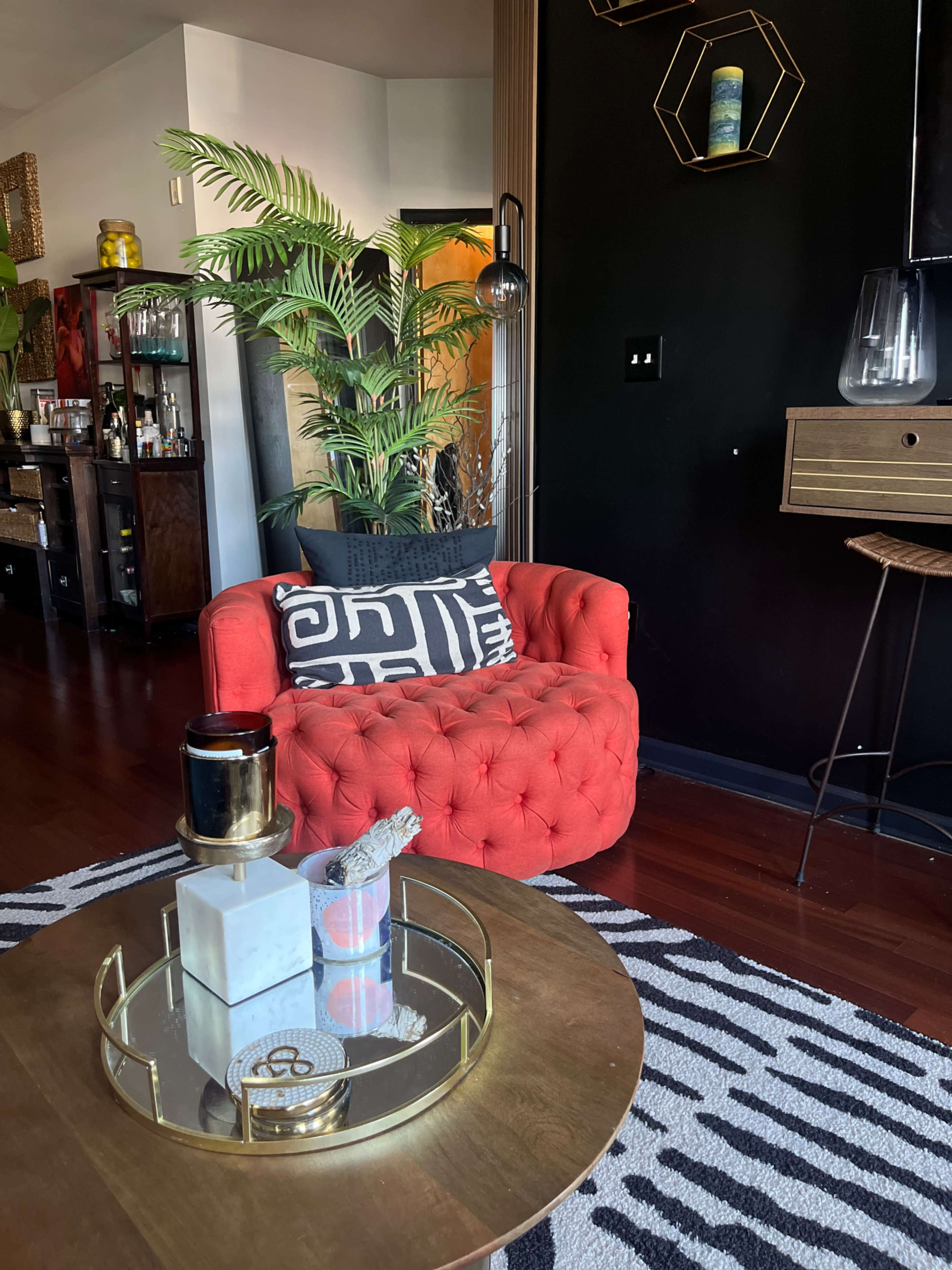 A bright red tufted armchair is positioned next to a round wooden coffee table on a zebra-striped rug in a stylish interior.