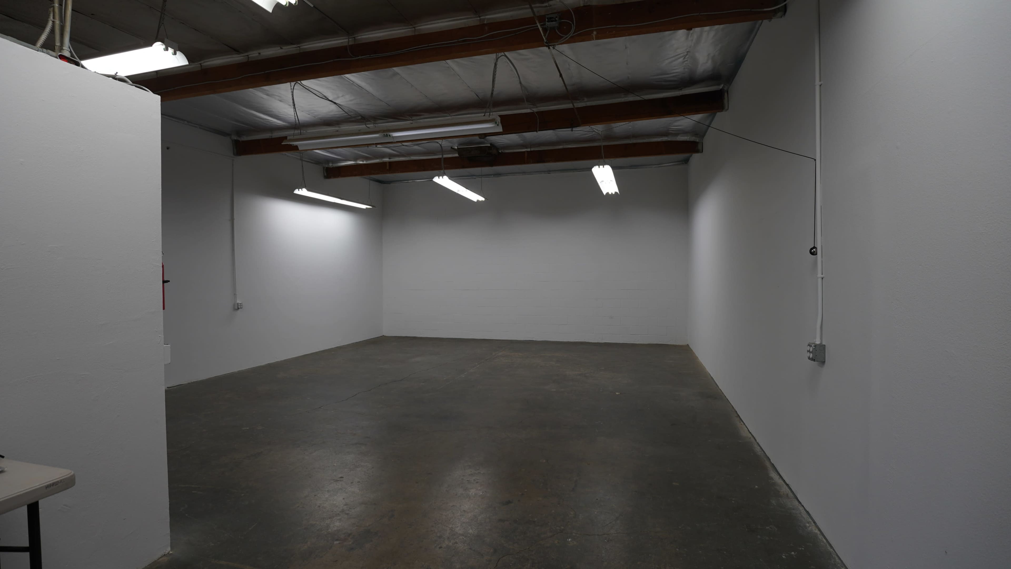 The image shows a vacant industrial room with plain white walls, a concrete floor, and overhead fluorescent lighting.