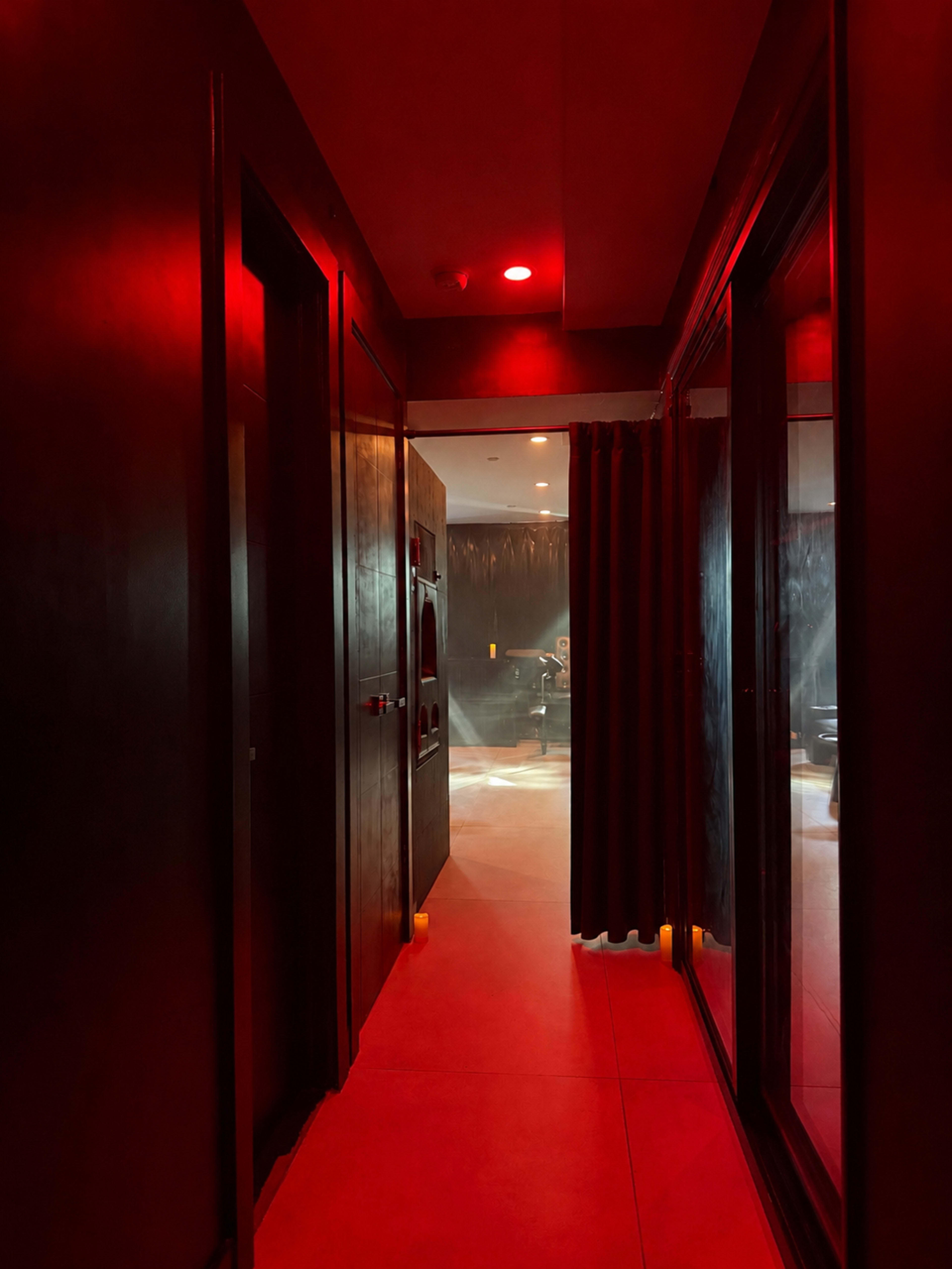 The image shows a dimly lit hallway with red lighting and glass doors on either side.