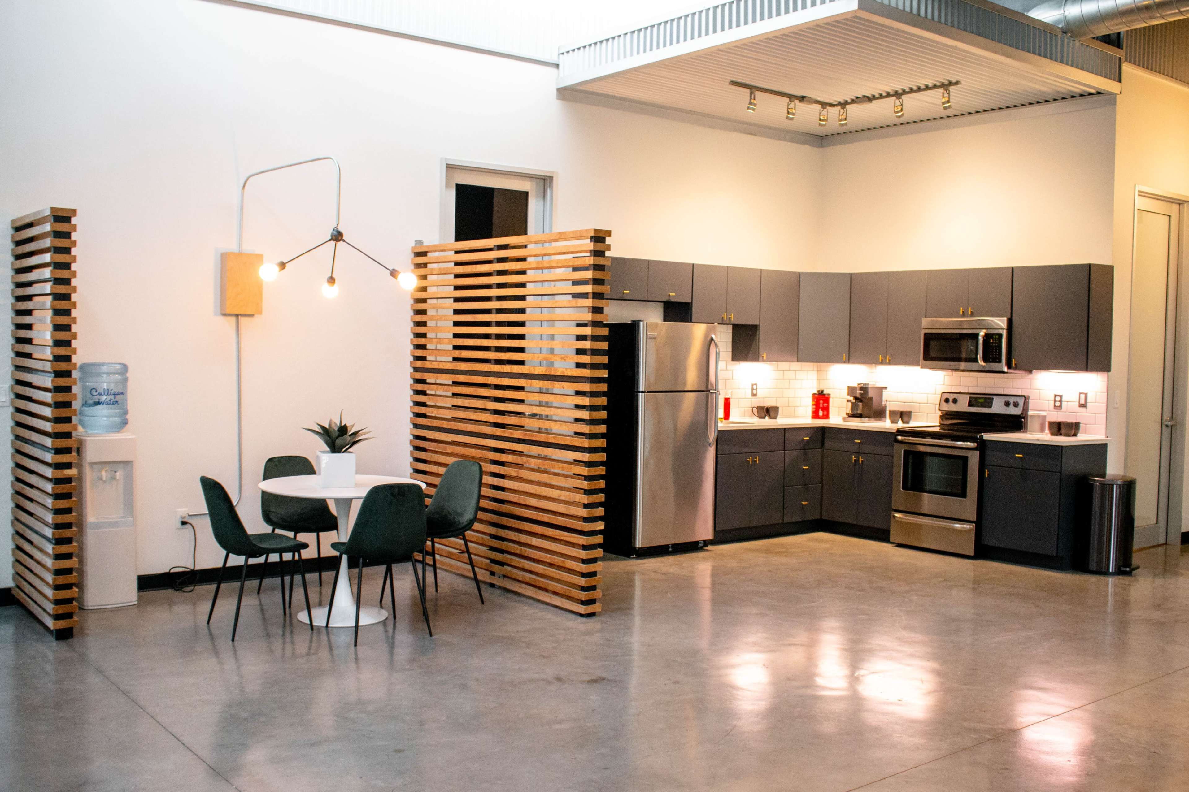 A modern kitchen with stainless steel appliances and a dining area featuring a round table and green chairs, separated by wooden partitions.