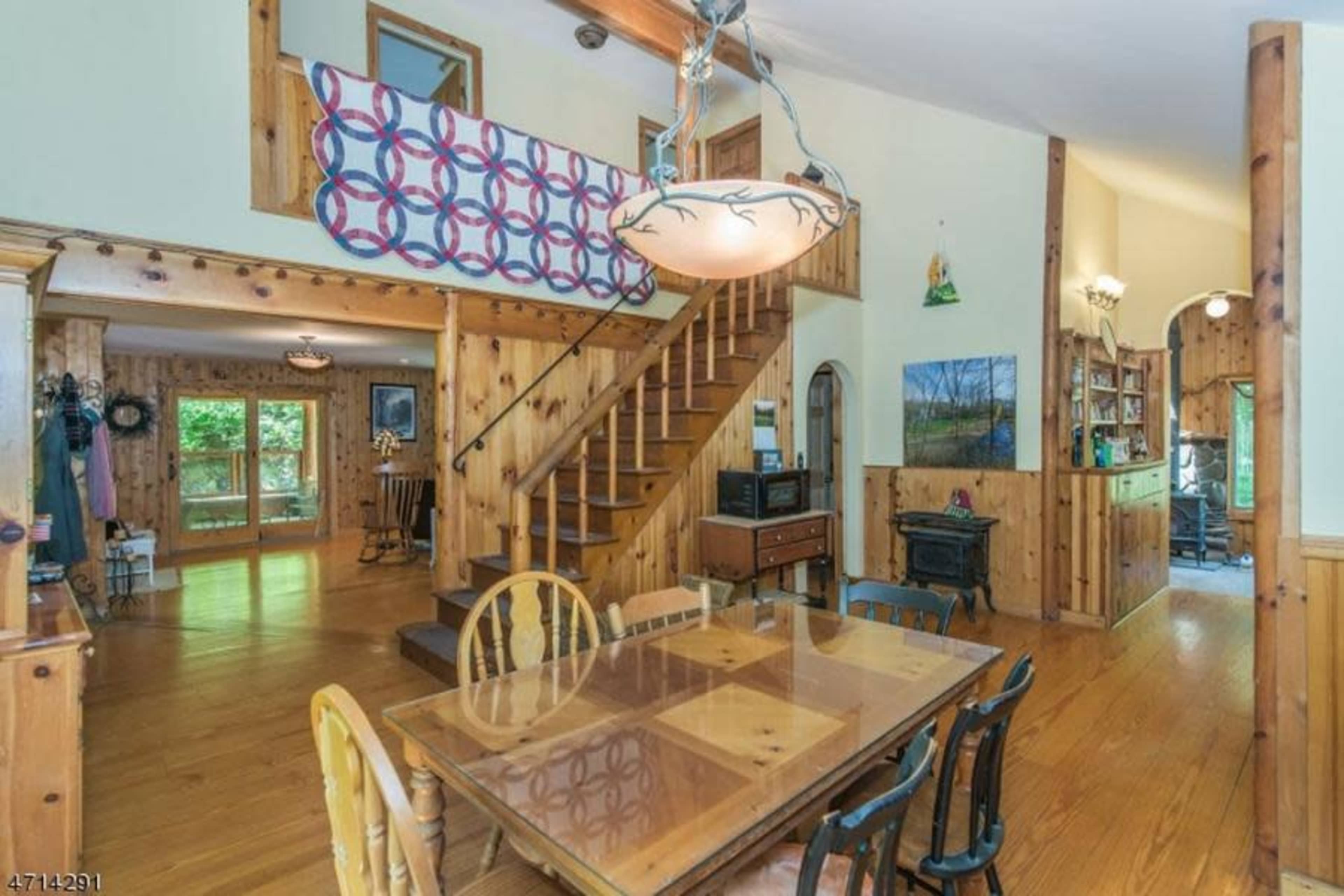 A wooden-furnished dining area connected to a staircase, with natural light coming through large windows.