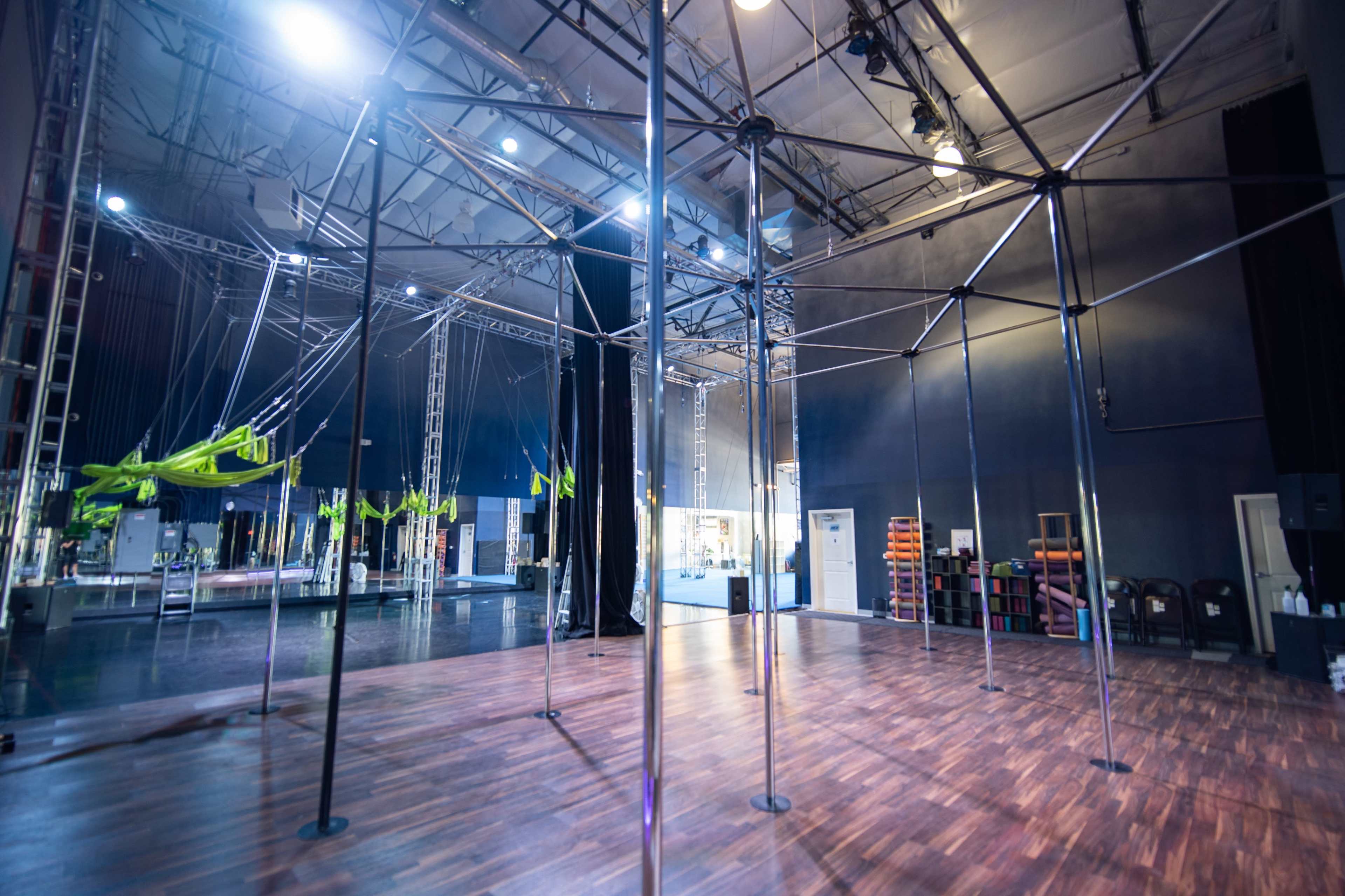 An empty performance space with vertical poles and aerial apparatus hanging from the ceiling.