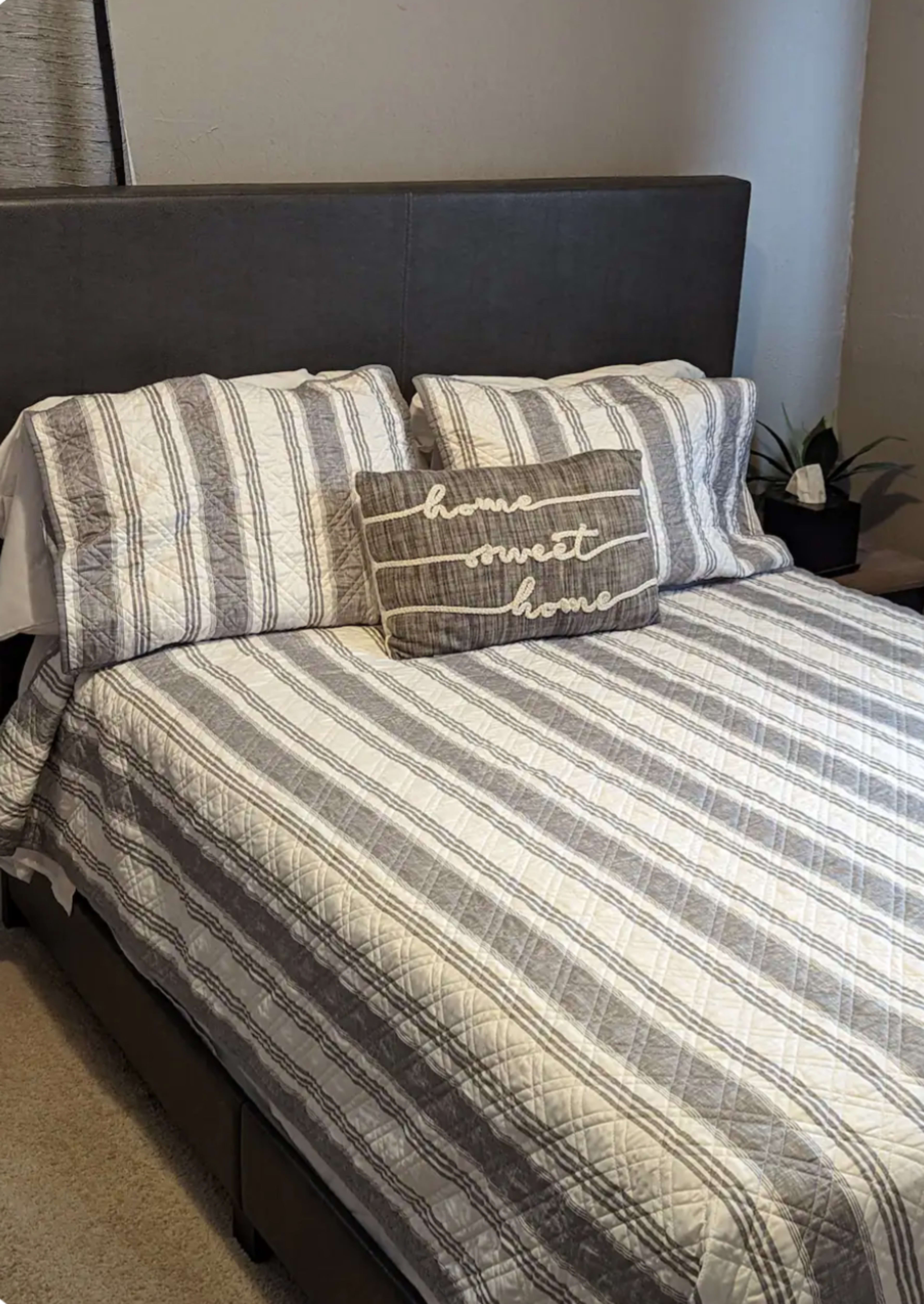 A neatly arranged bed with gray and white striped bedding and a decorative pillow that reads "home sweet home."