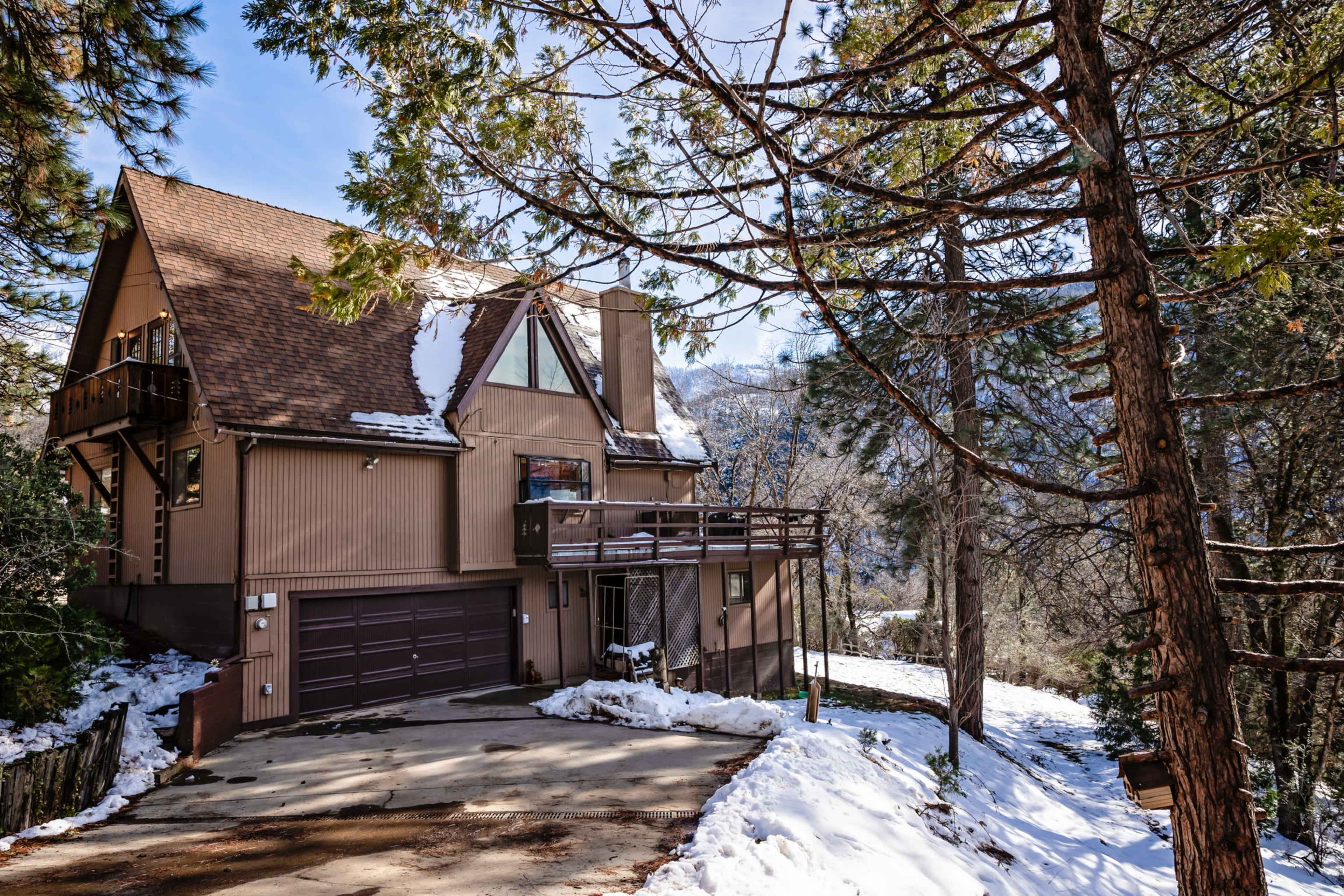 A large, A-frame mountain house surrounded by snow-covered ground and tall trees.