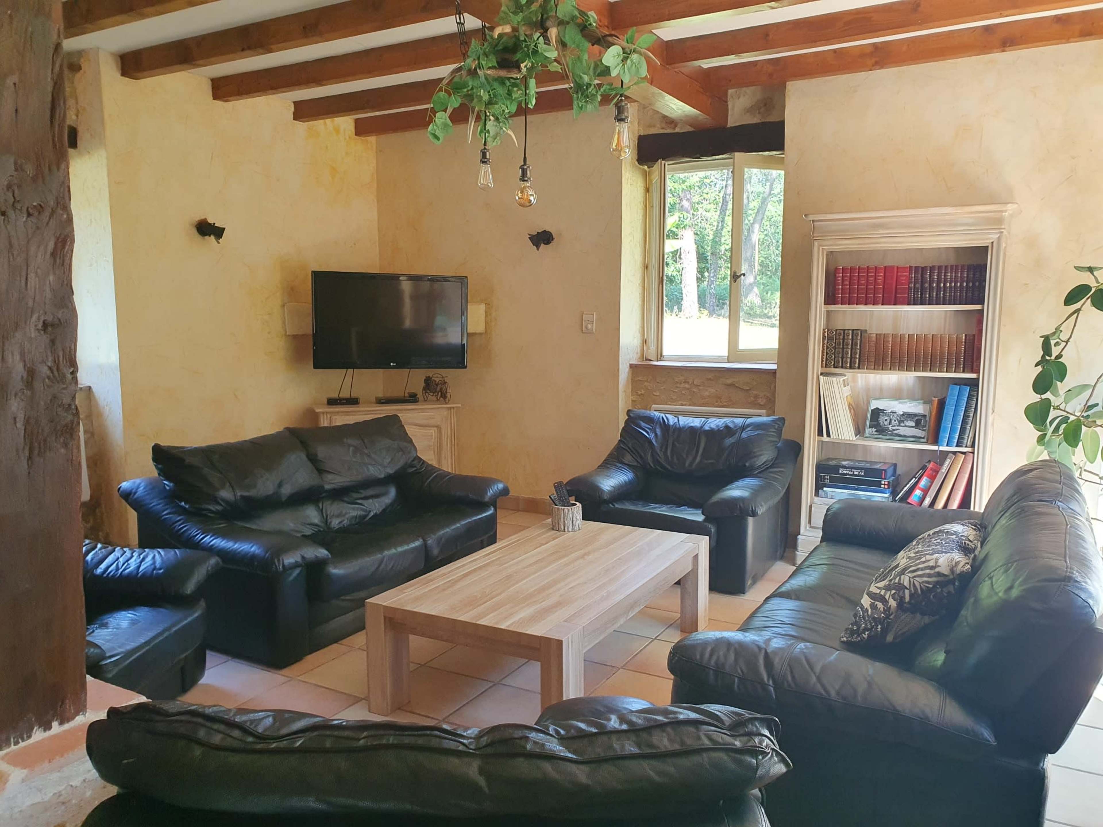 The image shows a living room with black leather furniture, a wooden coffee table, and a television against a cream-colored wall.