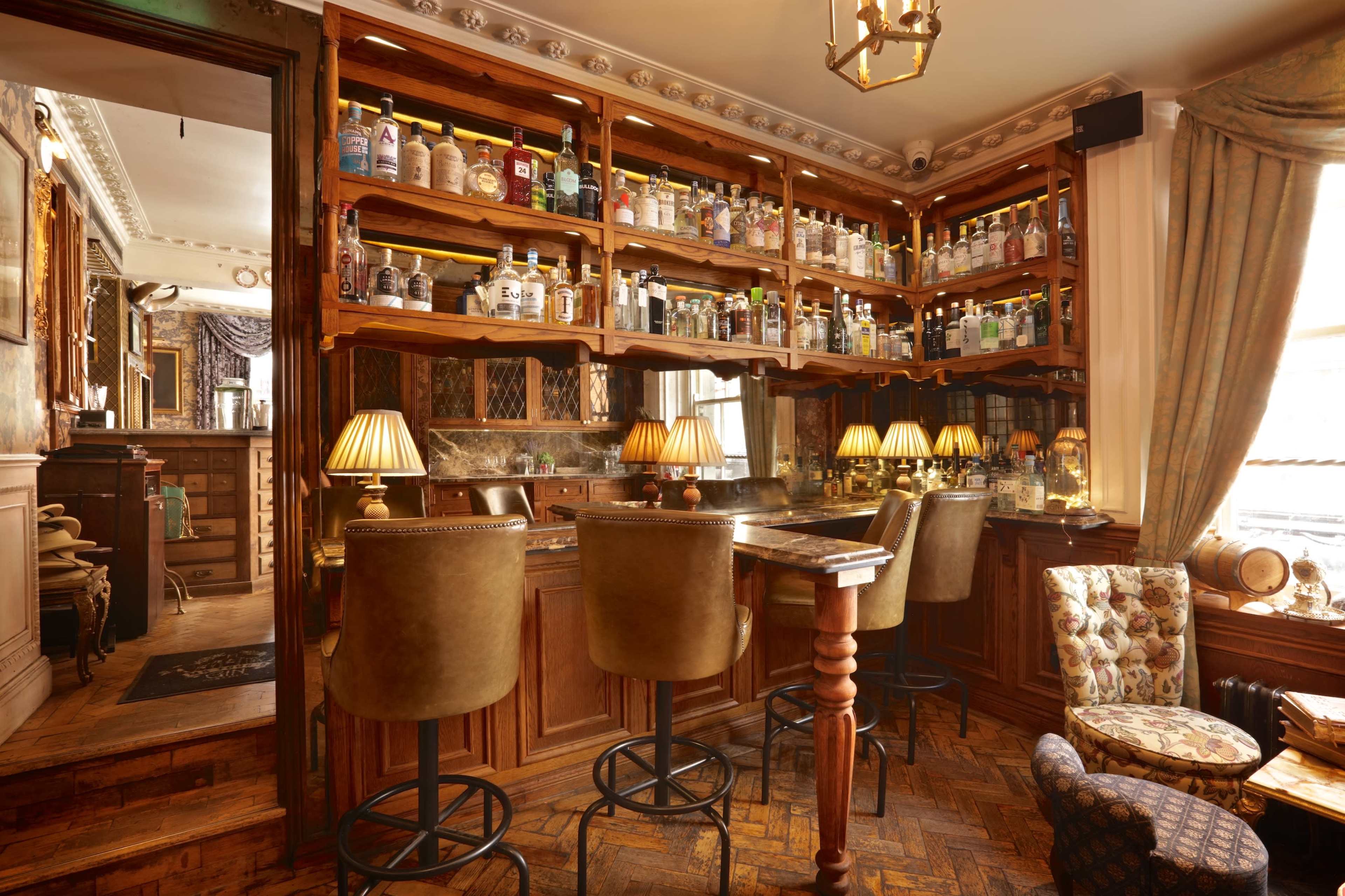 A cozy bar area with wooden shelves filled with various bottles and a few bar stools in front of a small table.