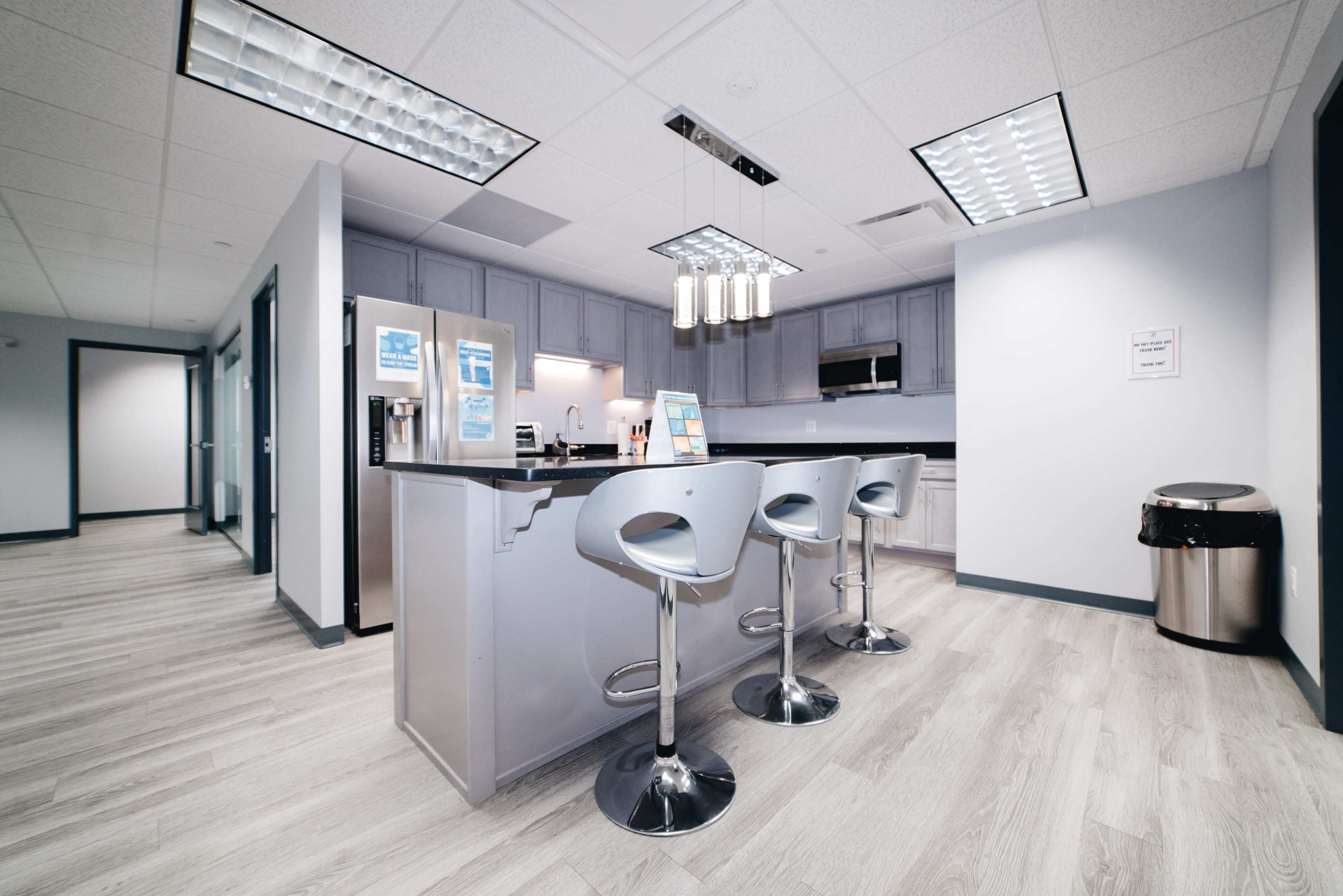 The image shows a modern kitchen area with gray cabinetry, a central island with three bar stools, and stainless steel appliances.
