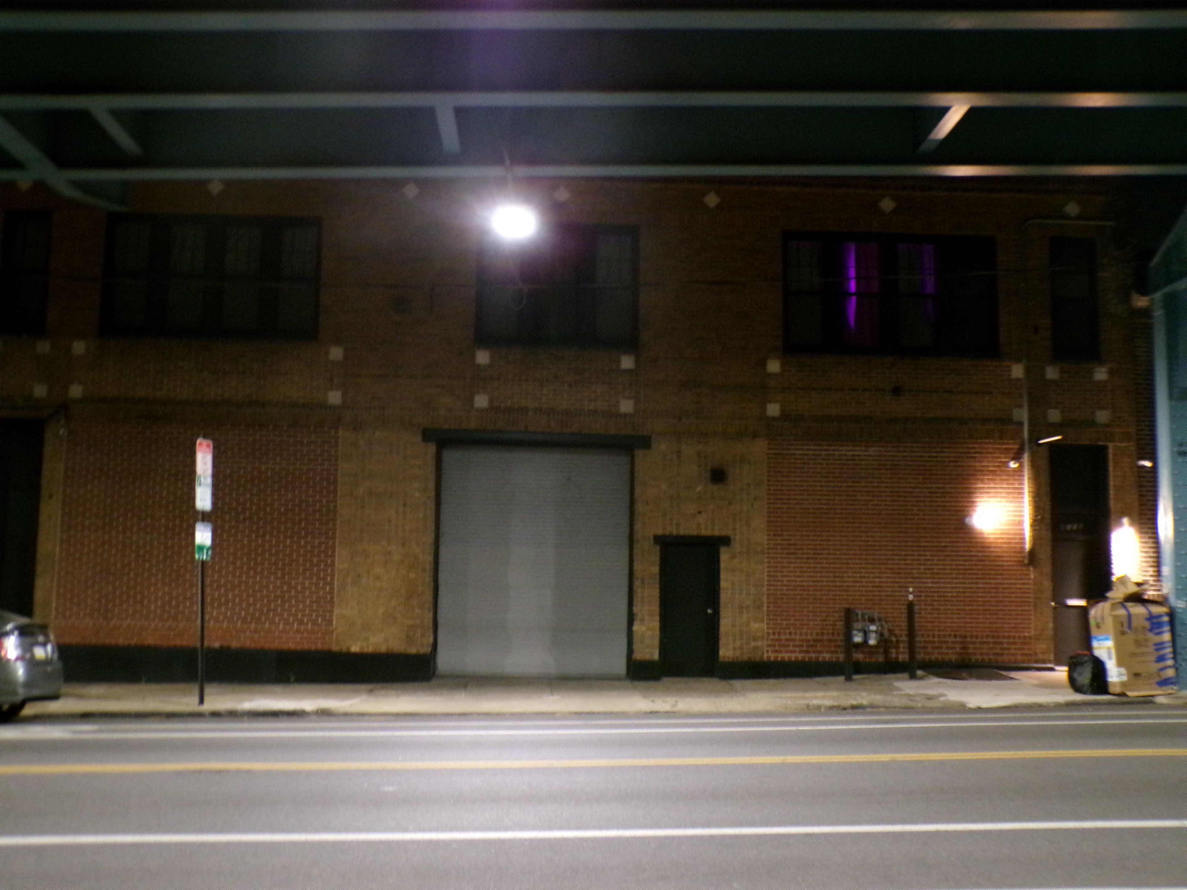 The image shows a brick building at night with a closed garage door and a dimly lit street.