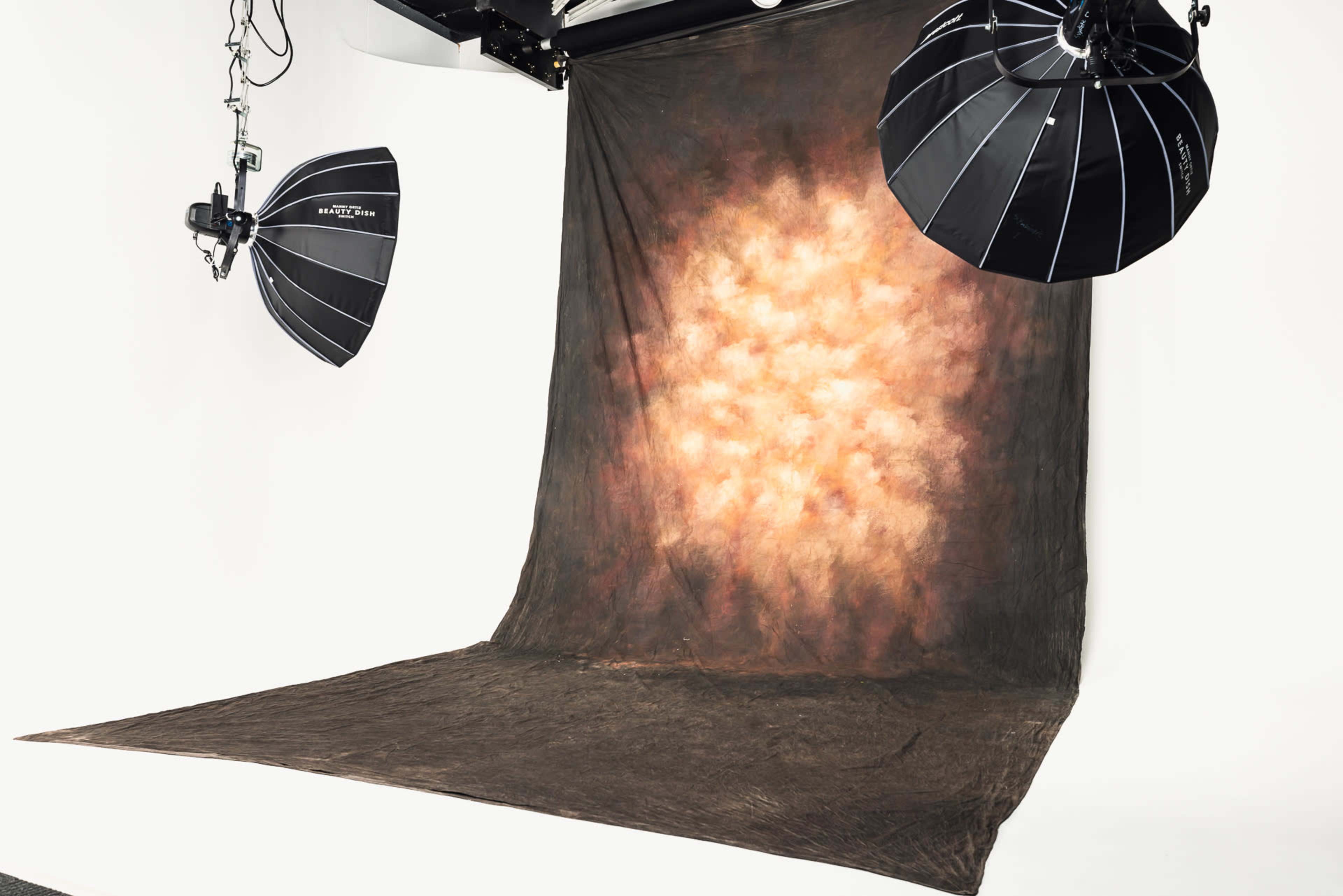The image shows a photography studio set up with a textured backdrop and two softbox lights positioned overhead.