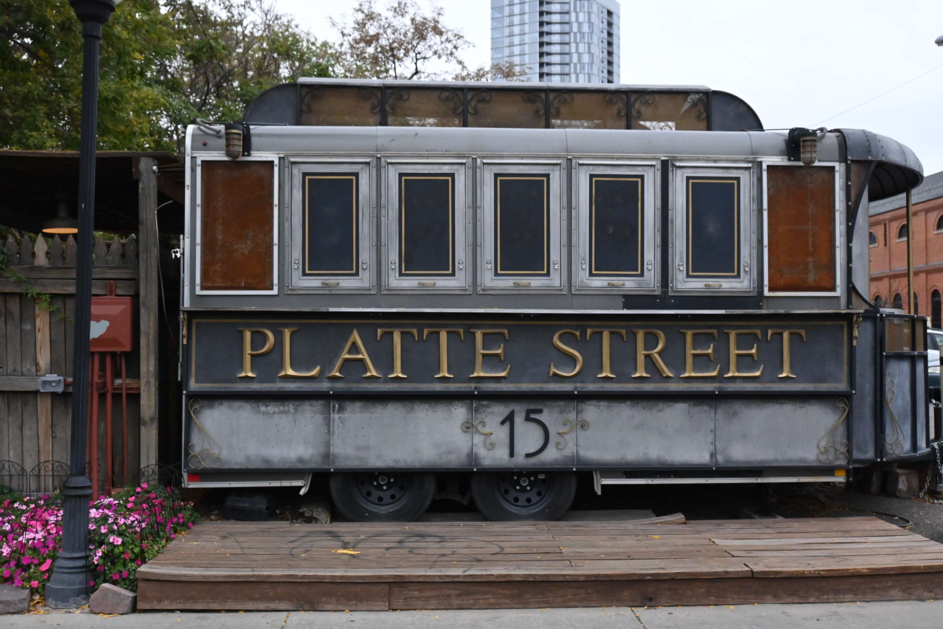 The image shows a vintage-style food truck with the name "Platte Street" prominently displayed on its side, parked near a wooden deck and surrounded by flowers.