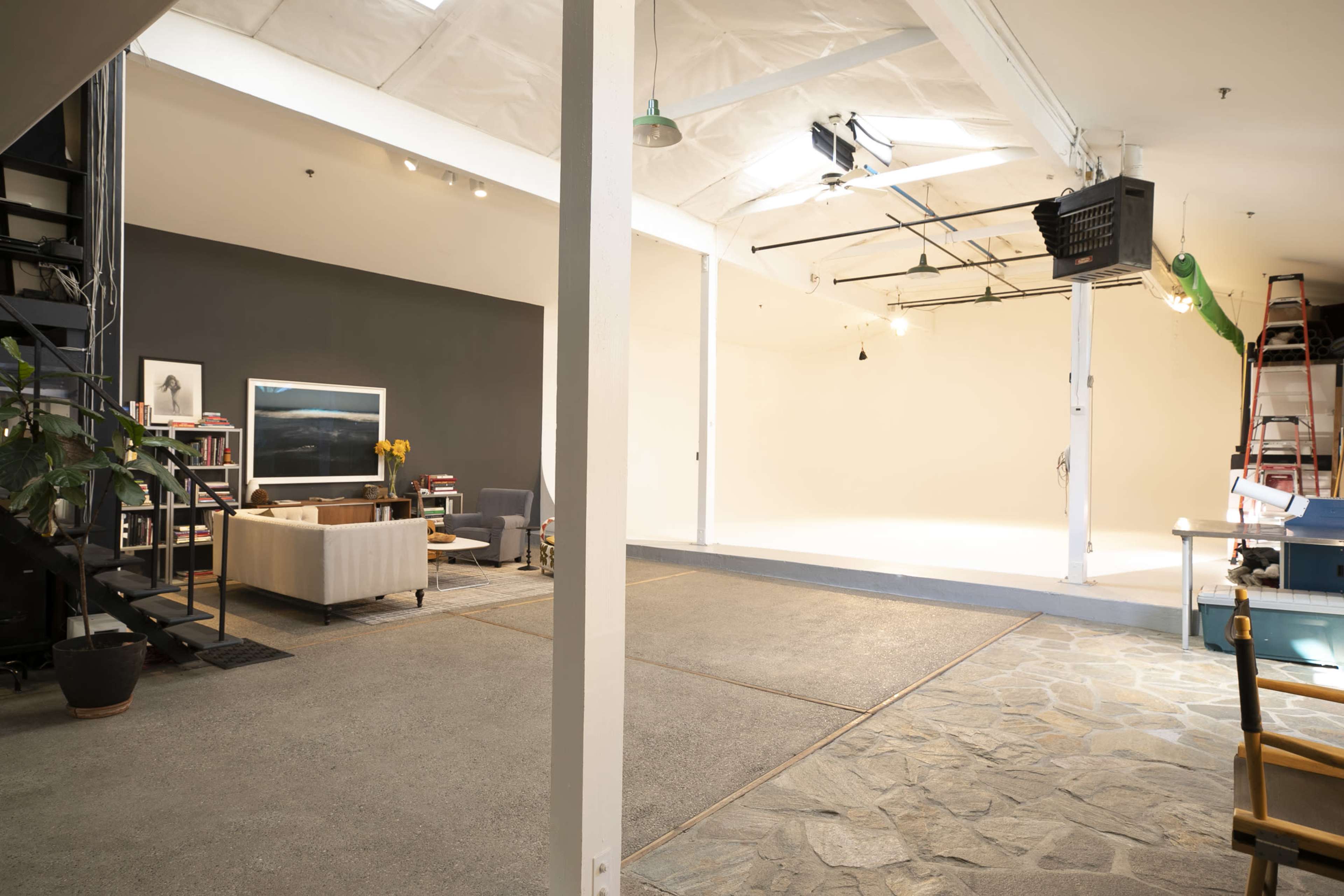 An industrial-style studio space with a dark wall, seating area, and a light-colored backdrop on the opposite side.