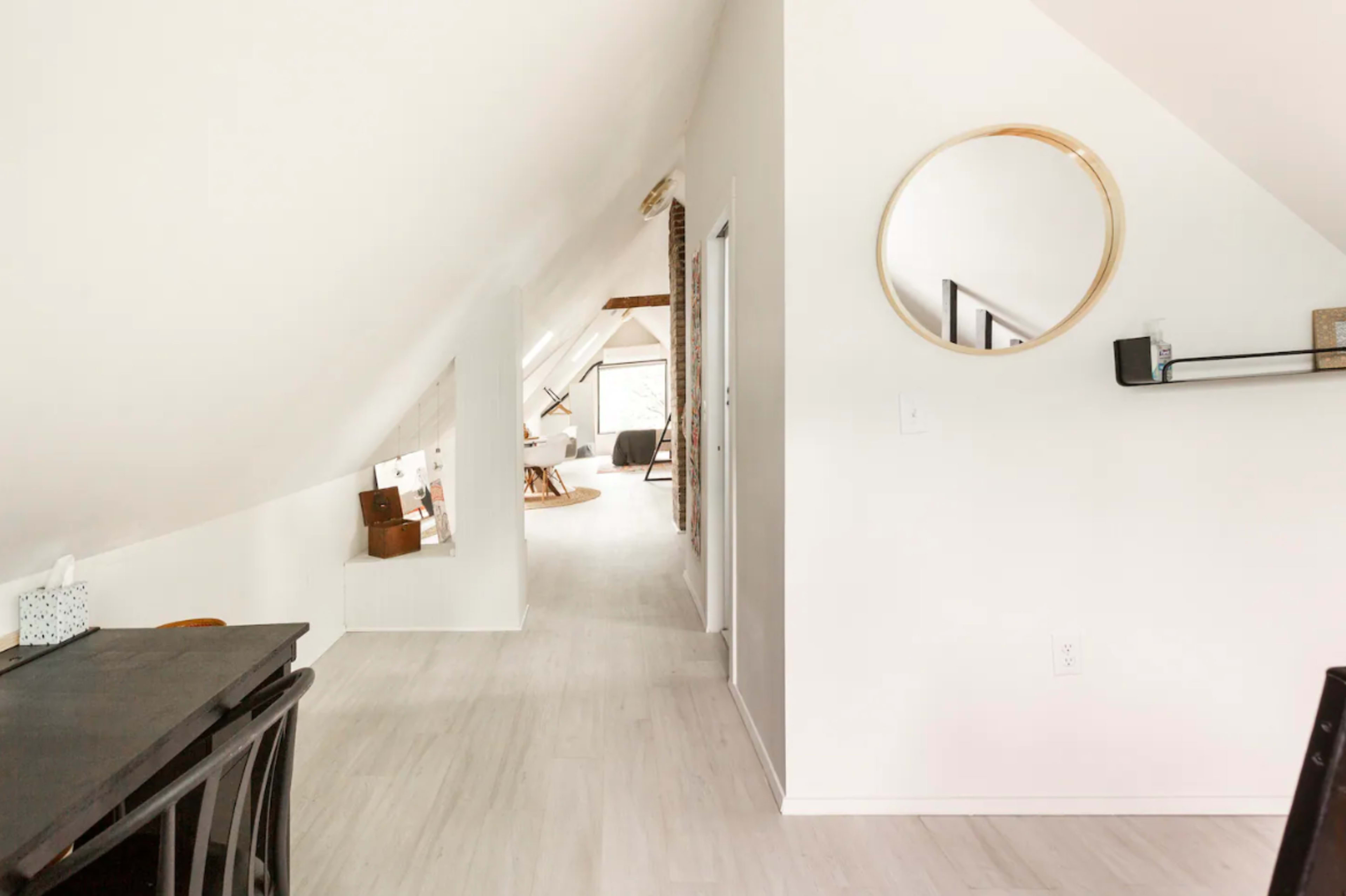 A bright, modern hallway with a high, sloped ceiling and a circular mirror on the wall.