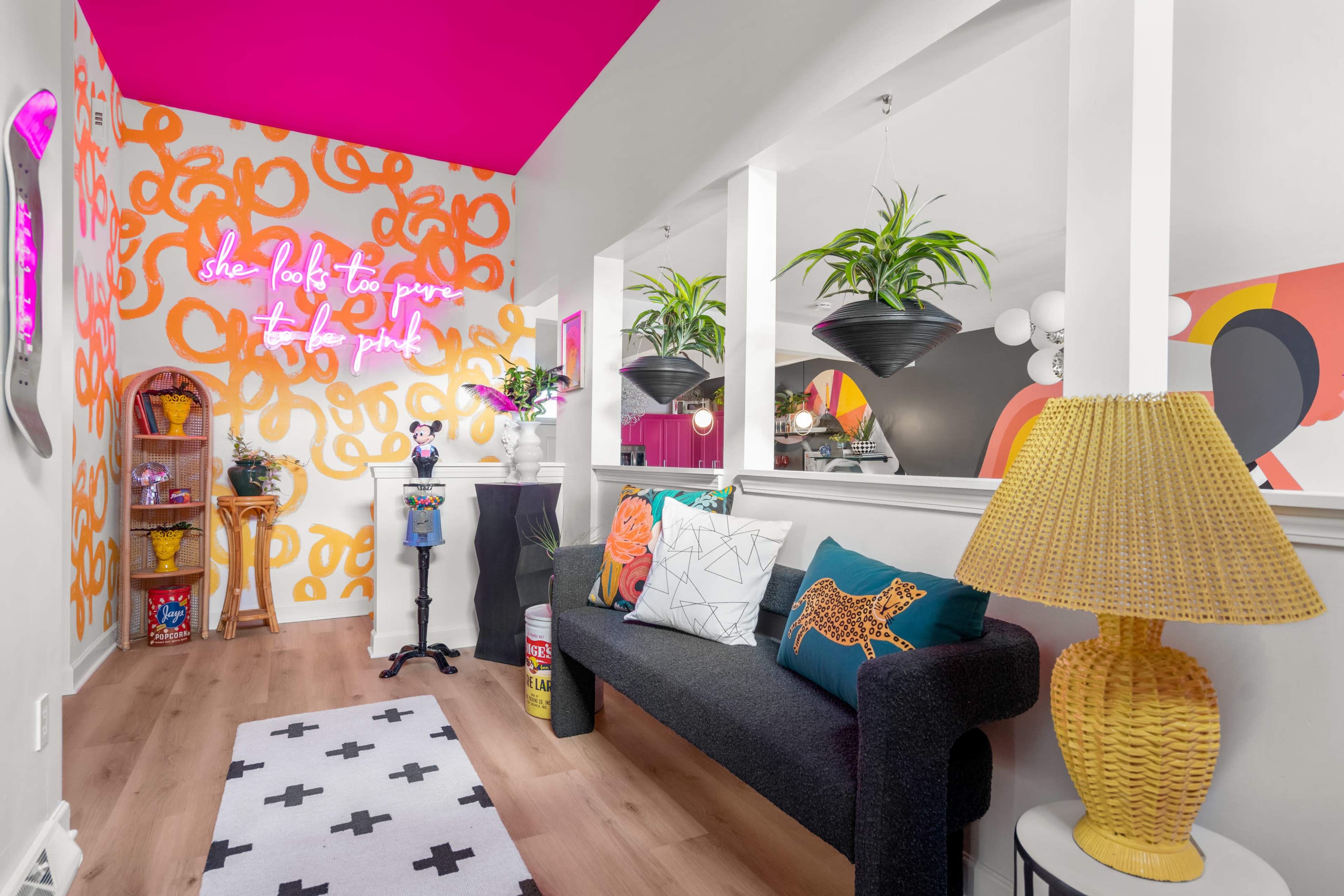 A brightly decorated room featuring a black sofa, colorful wall art with neon text, and plants in hanging planters.