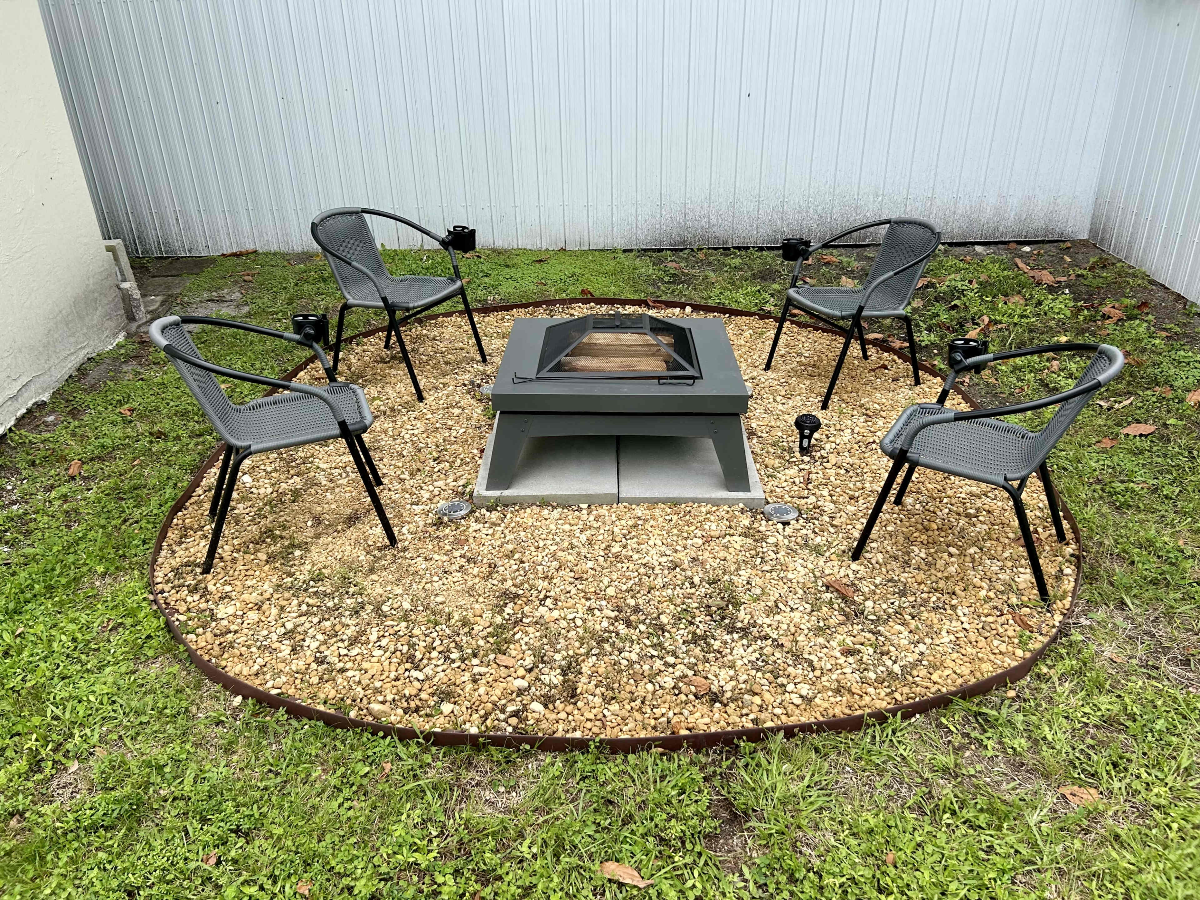 A circular gravel area features a fire pit surrounded by four chairs.