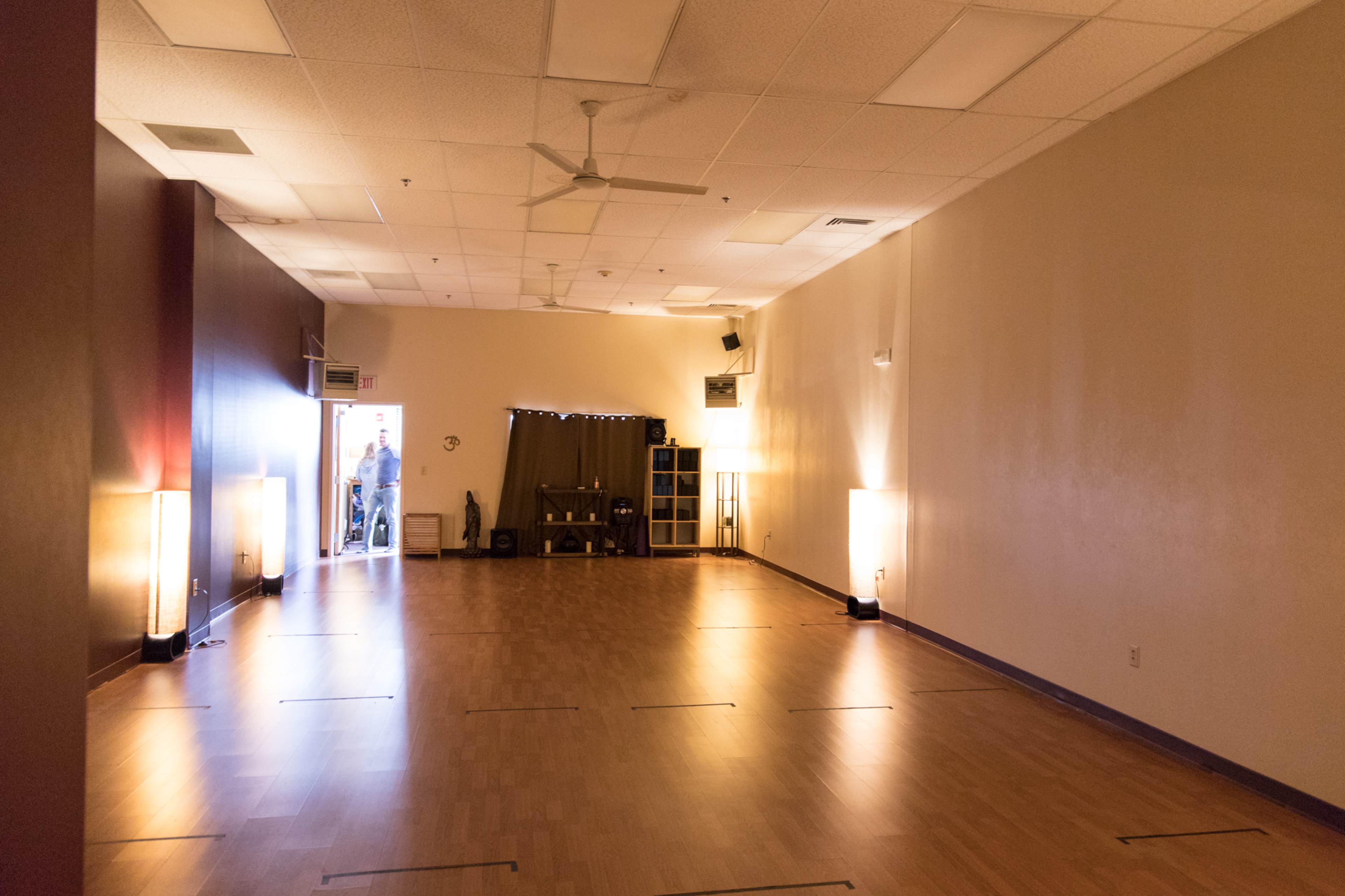 A spacious indoor room with wooden flooring, lit by floor lamps, and an entrance leading to another area.