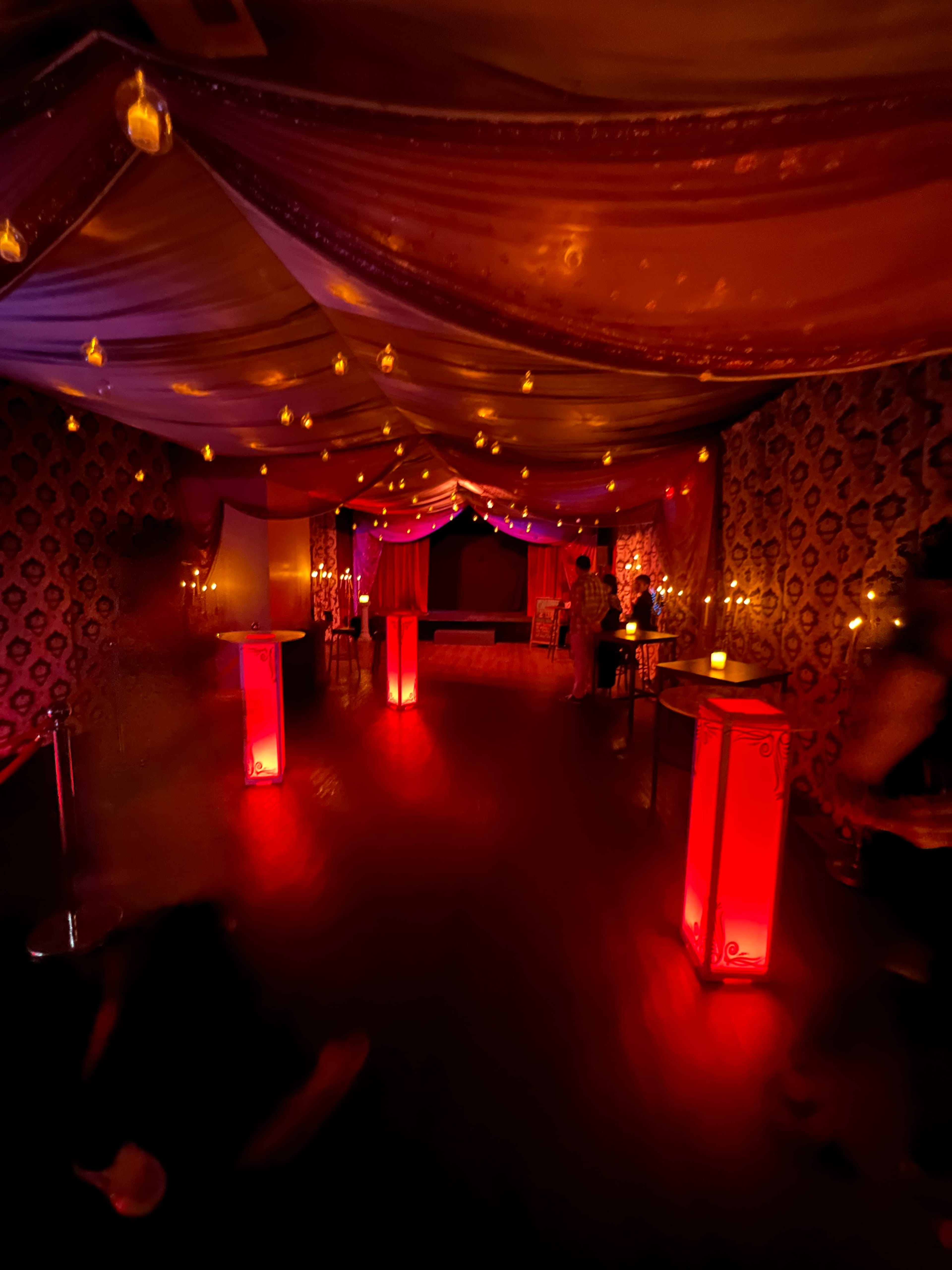 The image shows a dimly lit room with red and purple drapery, ambient lighting, and decorative lanterns, creating a vibrant atmosphere.