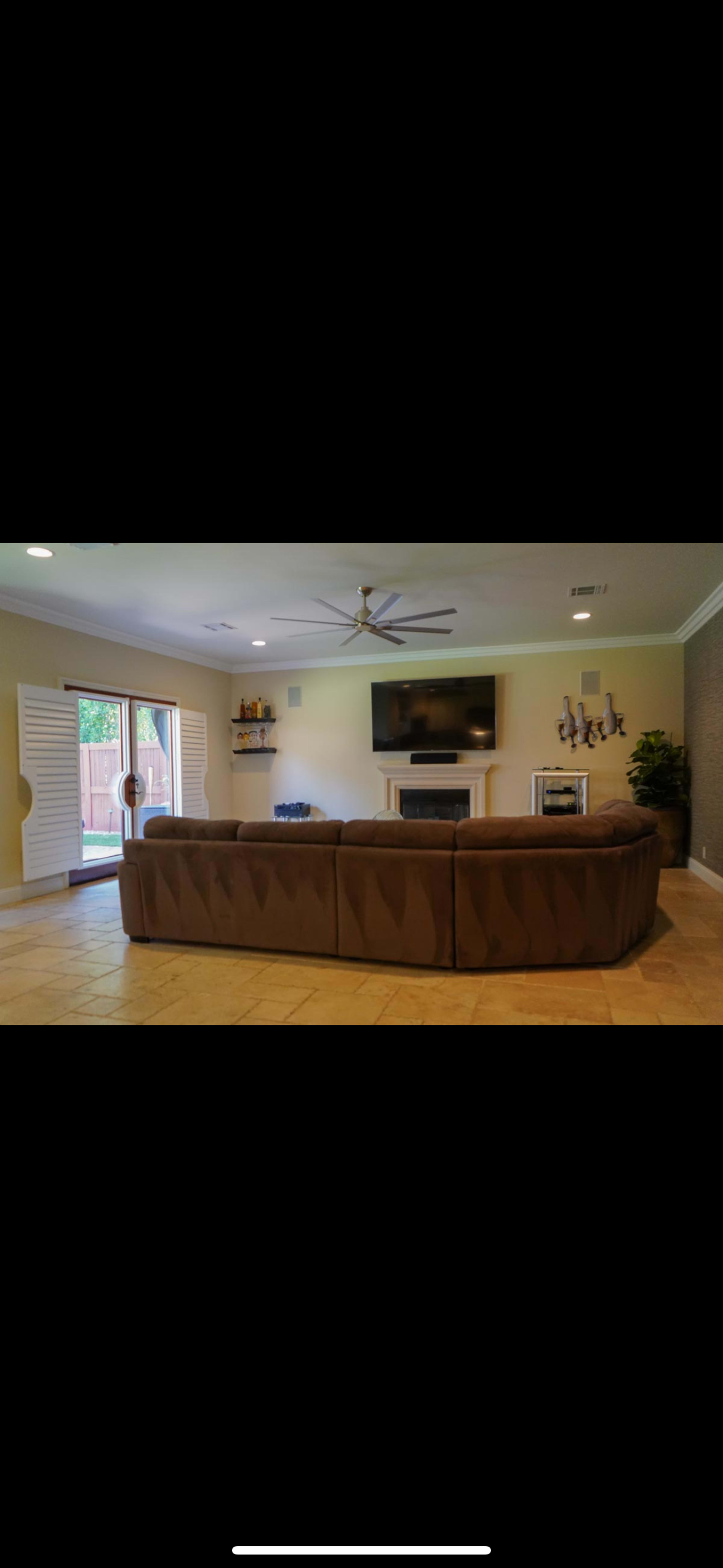 A spacious living room features a large sectional sofa, a television mounted on the wall, and sliding glass doors leading to an outdoor area.