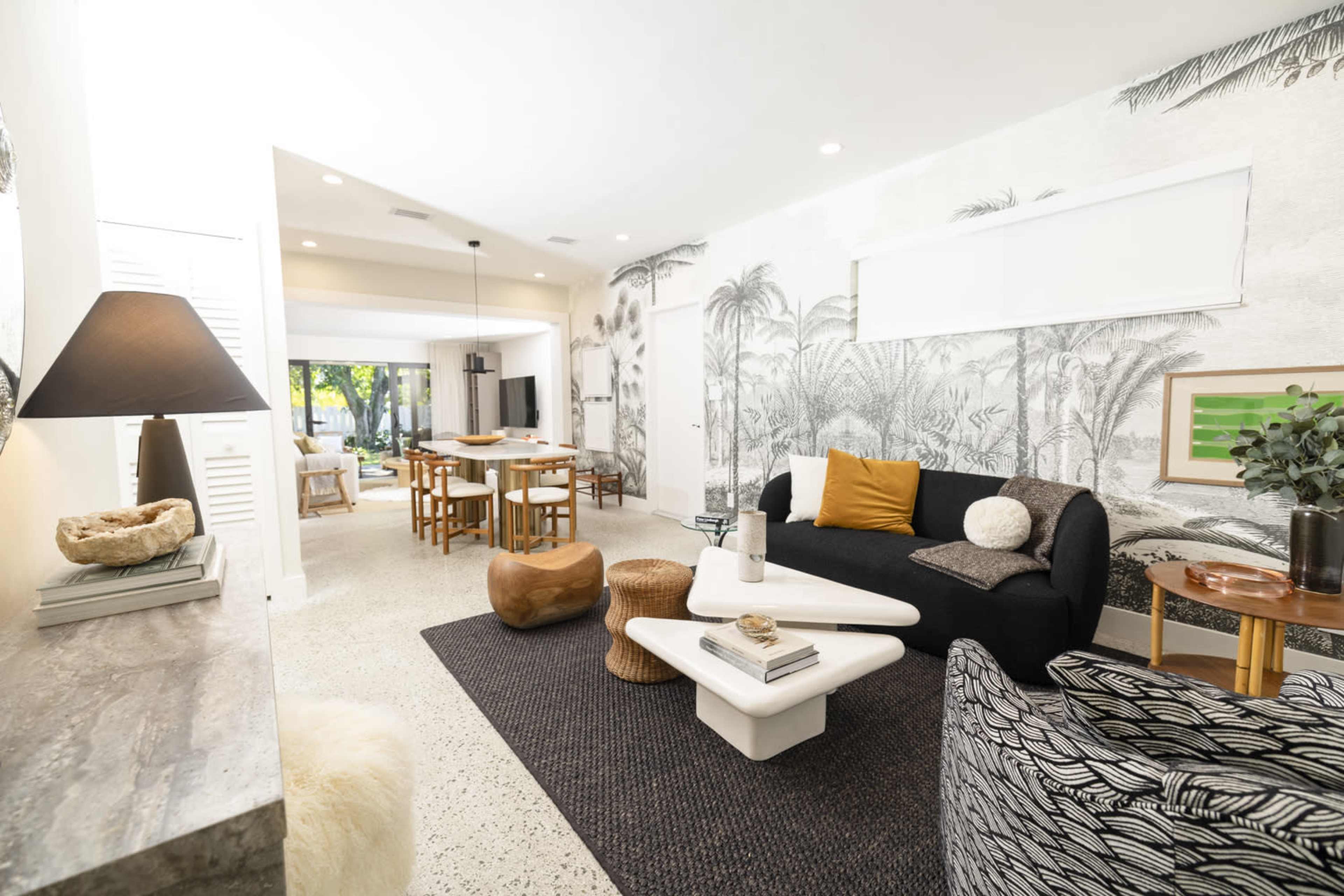 A modern living room features a black sofa, a coffee table, and decorative elements with an open layout that leads to a dining area.