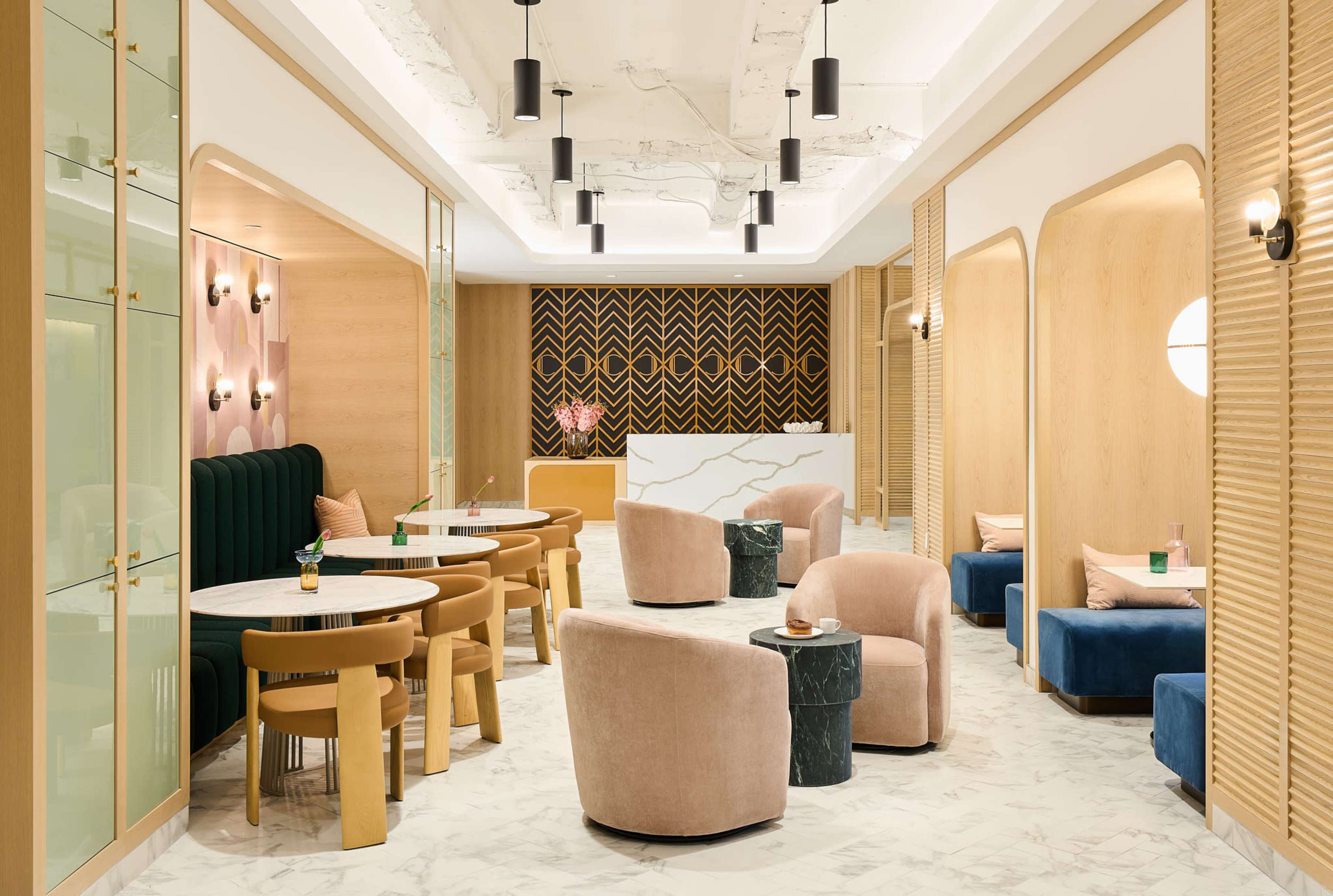 The image depicts a modern café interior featuring circular tables, plush seating in various colors, and geometric-patterned walls.