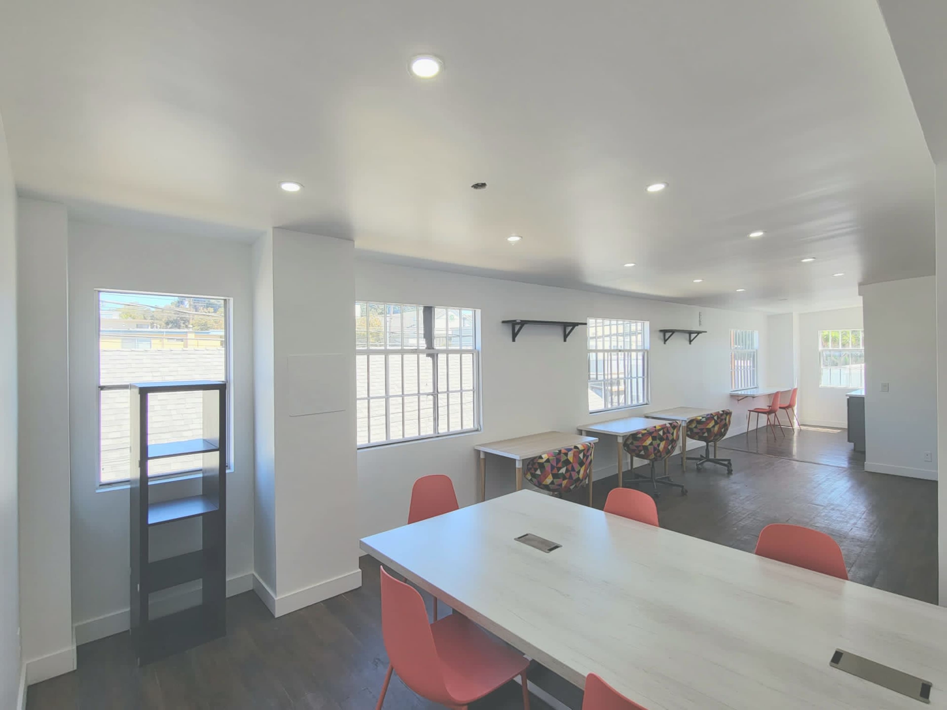 A bright, modern room with a long table and colorful chairs, featuring large windows that allow natural light to fill the space.