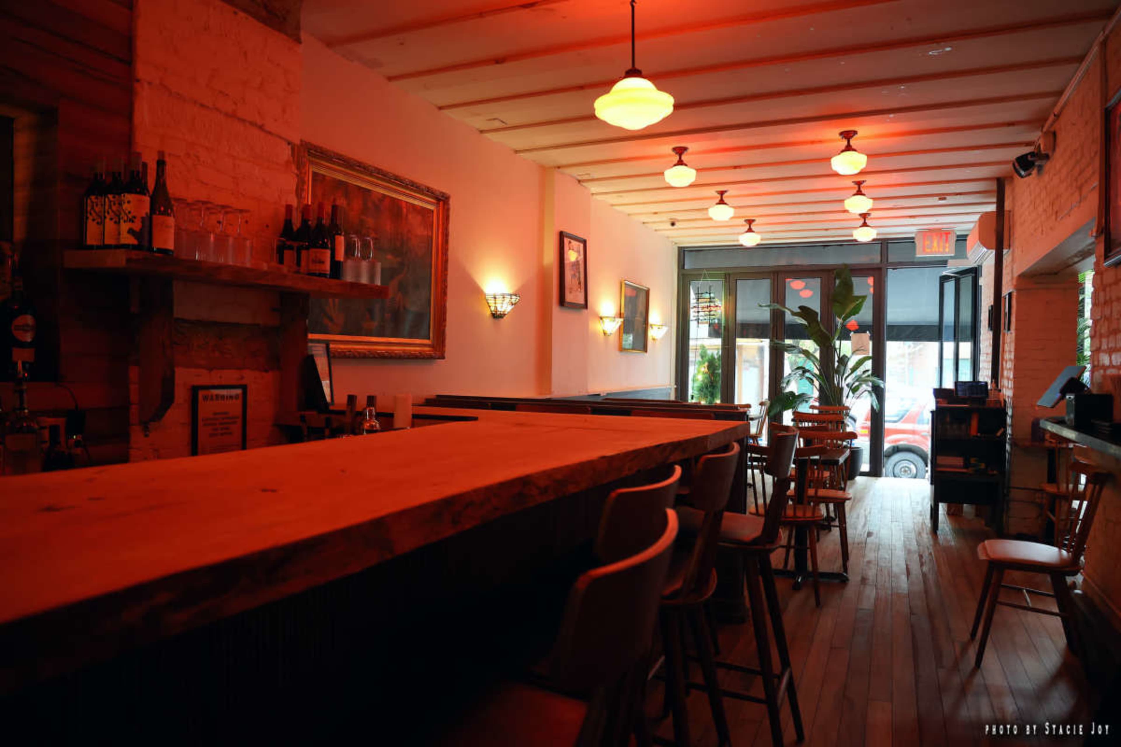 A dimly lit bar area features wooden seating and a long countertop with bottles displayed on the wall.