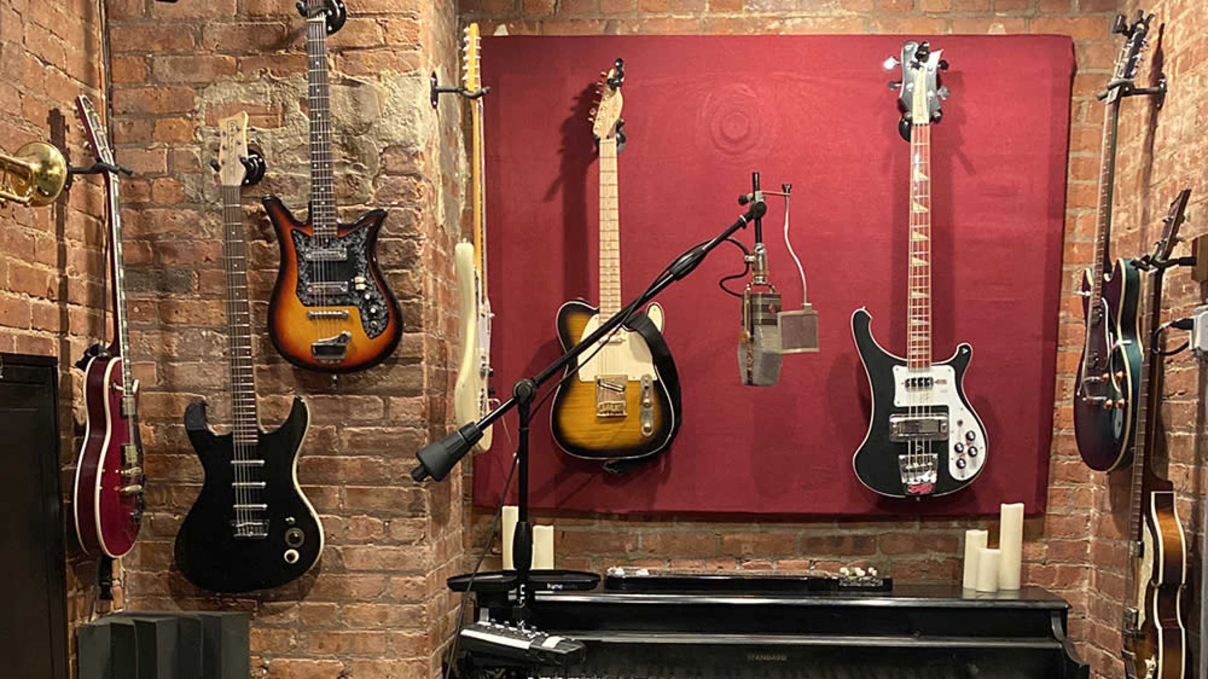 A brick wall with several guitars displayed on it and a microphone mounted on a stand in front of a piano.